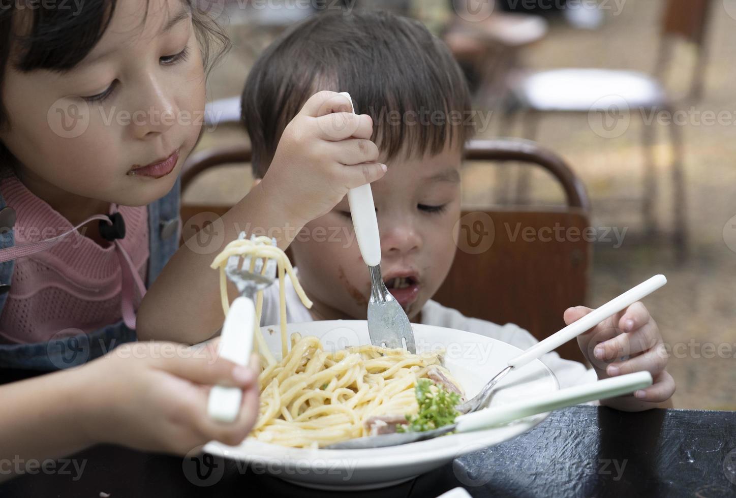 asiatische Jungen und Mädchen essen Spaghetti mit Köstlichkeit. Schwester und Bruder essen Spaghetti foto