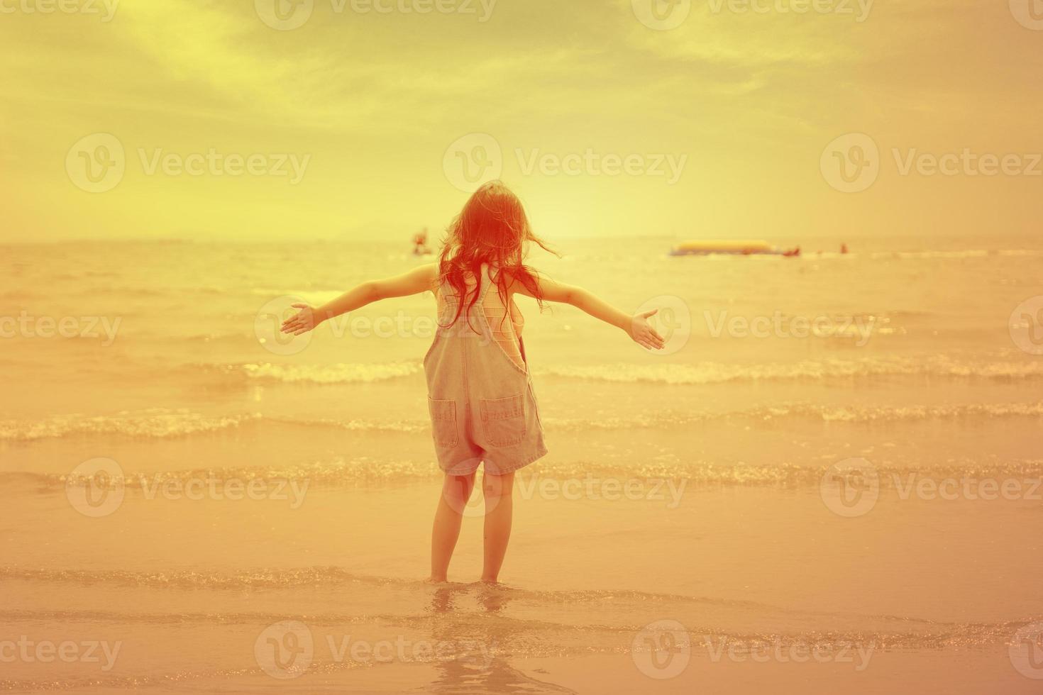 glückliches Kind, das bei Sonnenuntergang am Strand spazieren geht. entzückendes kleines Mädchen, das entlang des Meerwassers spielt. kindheit und freiheit sommertage konzept foto