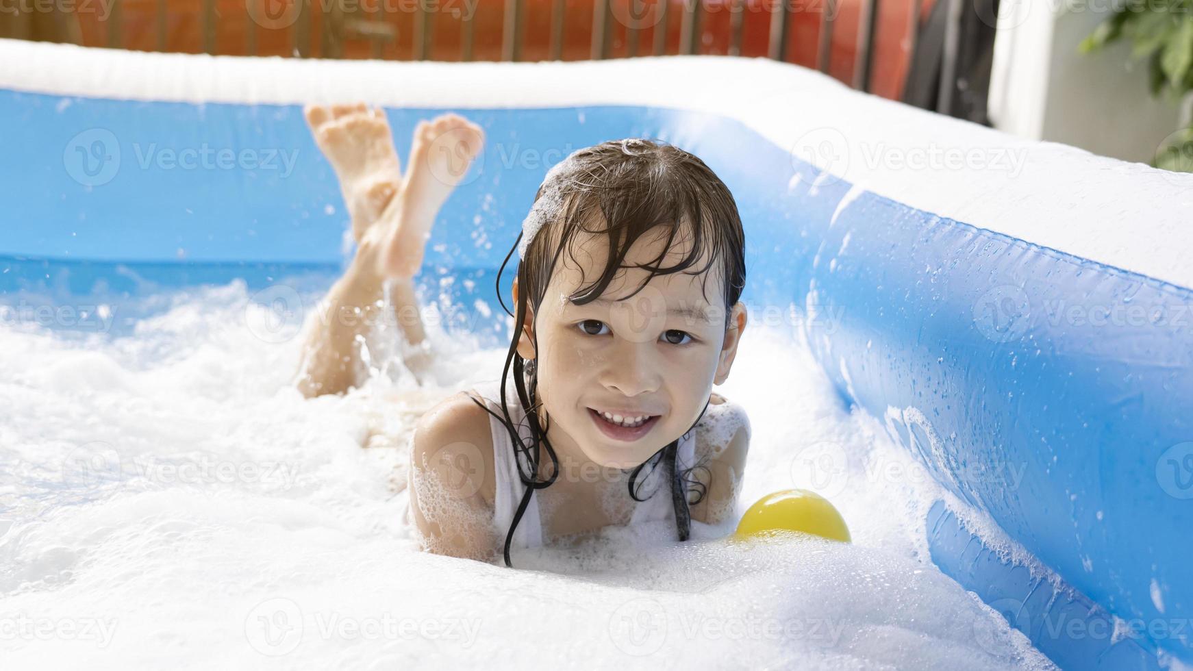 Schönes asiatisches Mädchen, das in einem aufblasbaren Pool spielt. im Sommer zu Hause im Wasser spielen. Seifenblasenspiel, Familienglück, im Wasser spielende Kinder foto