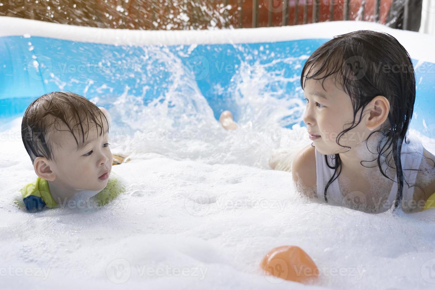 süße asiatische geschwister haben spaß im schwimmbad. schwester und bruder spielen mit blasen und schwimmen im sommerferienpool. glückliches familienurlaubskonzept foto
