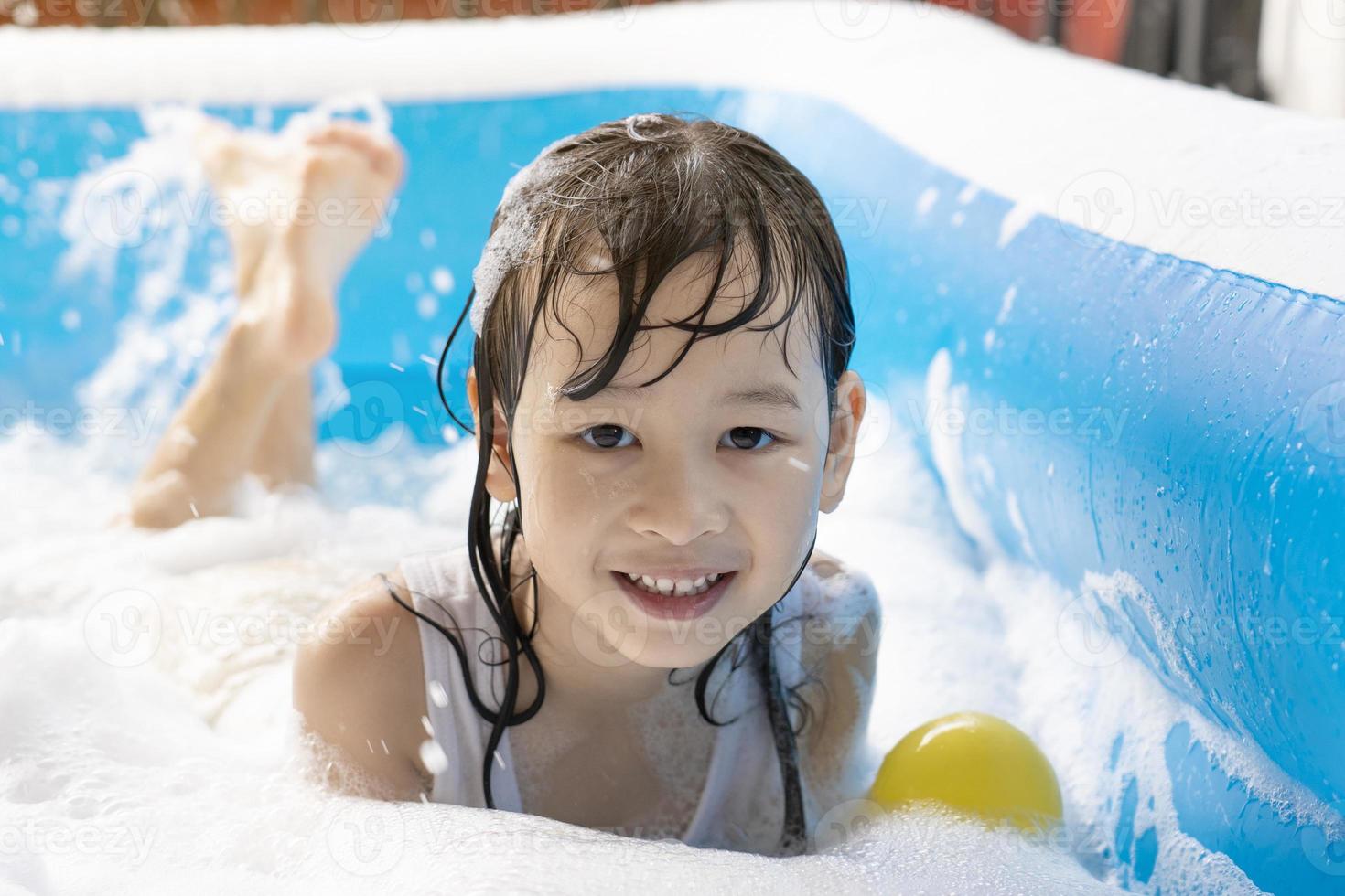 Schönes asiatisches Mädchen, das in einem aufblasbaren Pool spielt. im Sommer zu Hause im Wasser spielen. Seifenblasenspiel, Familienglück, im Wasser spielende Kinder foto