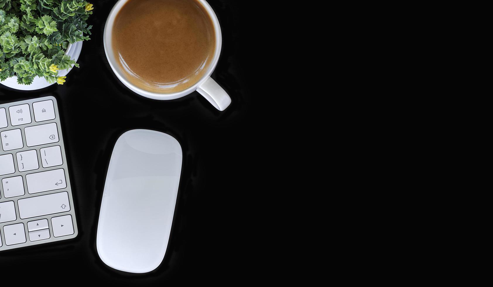 Draufsicht des Arbeitsbereichs mit einer Tastatur, einer Maus und einem Kaffee auf einem schwarzen Tisch foto