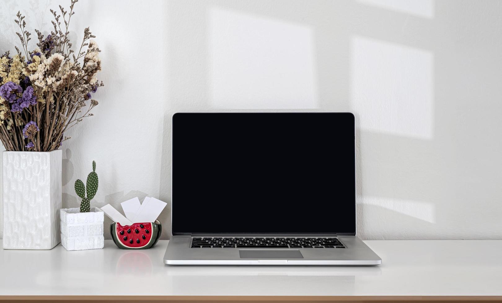 Laptop mit leerem Bildschirm auf einem Schreibtisch mit Blumen foto