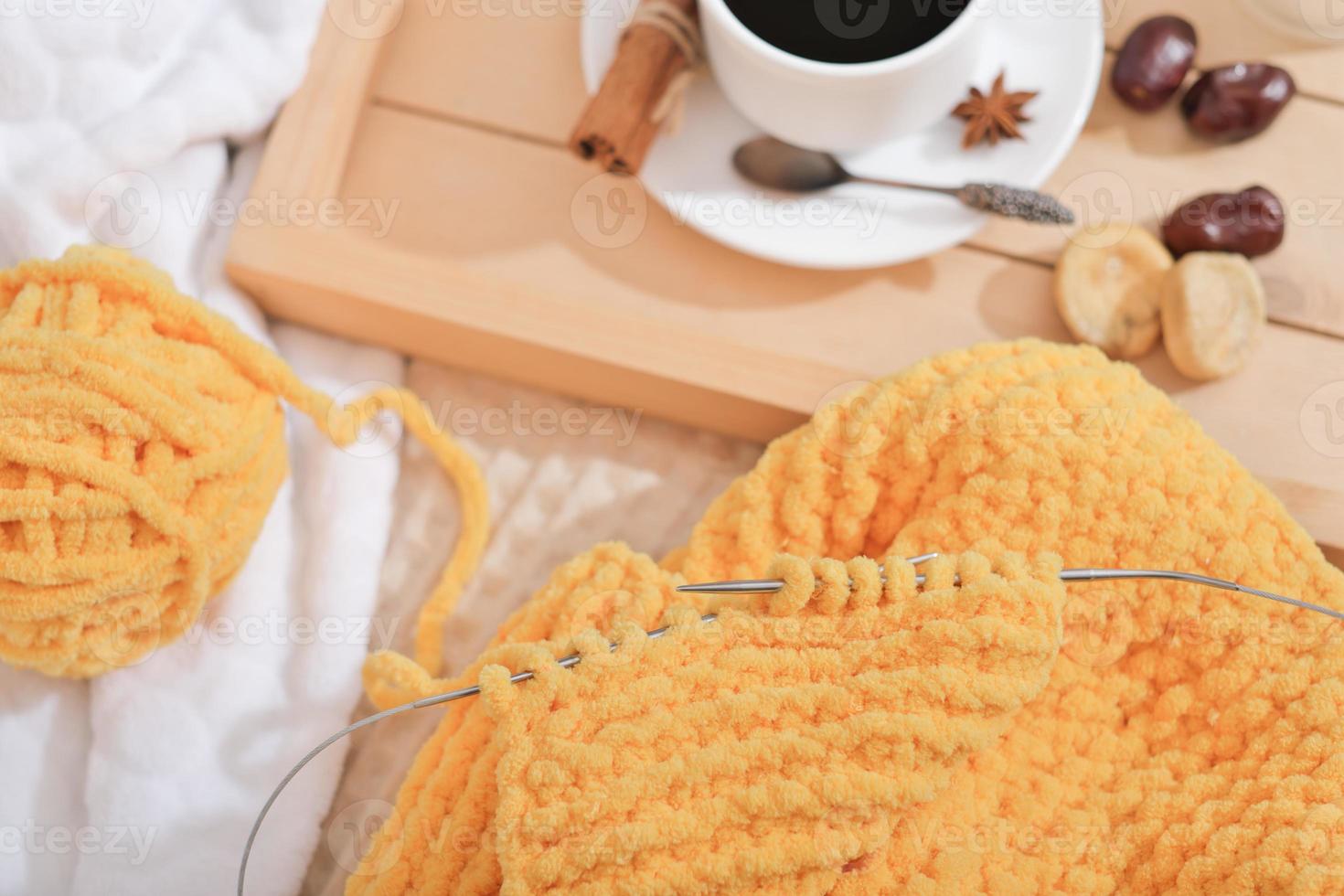 Strickschal mit Nadeln aus gelbem Garn. Zimtkaffee in einer weißen Tasse und Trockenfrüchten. Herbst- und Winterhobby. Schal in Arbeit. foto