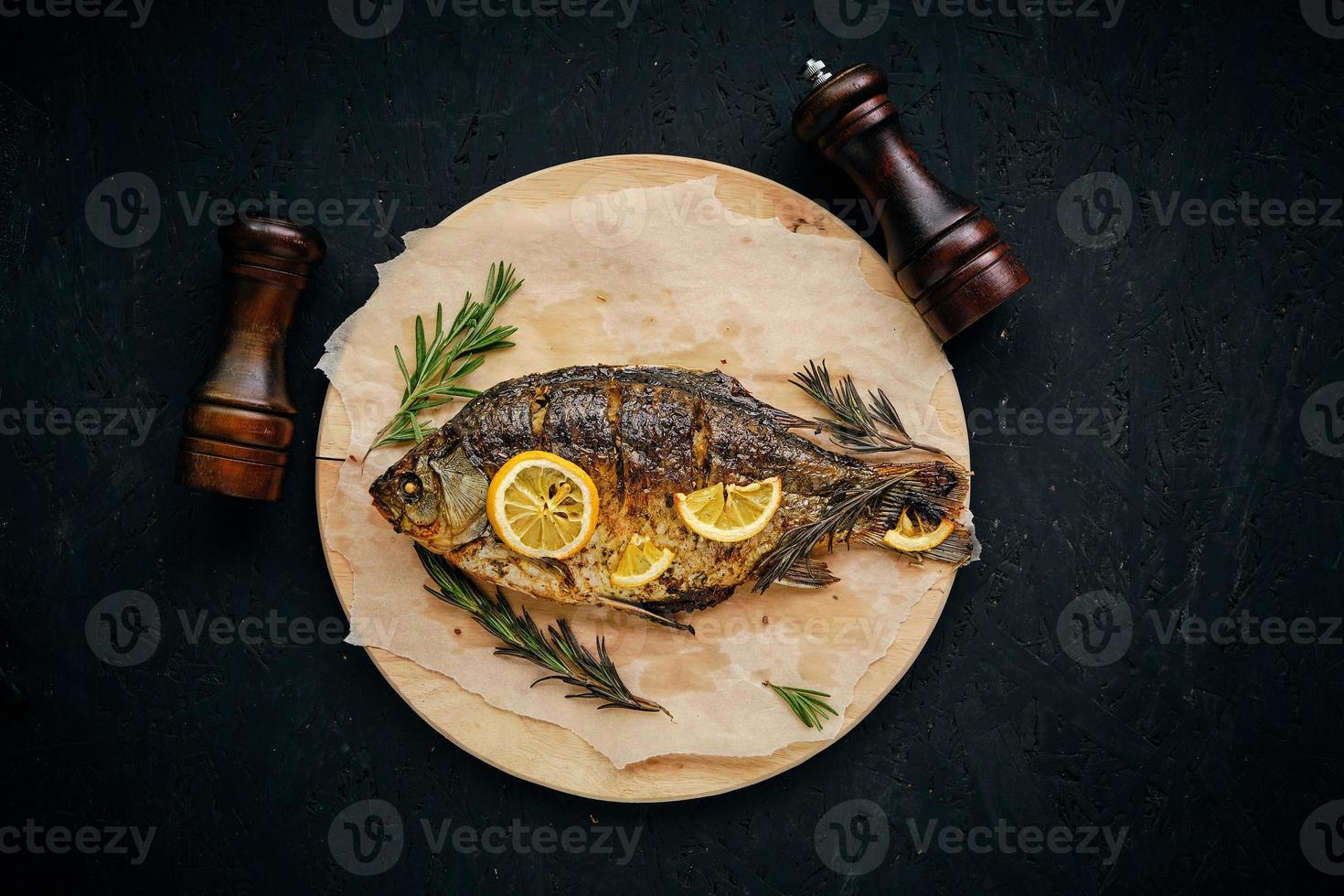 gebackener fisch im ofen mit zitrone und rosmarin ausgelegt schneidebrett und pergamentpapier. auf dunklem hintergrund mit zwei strohhalmen. foto