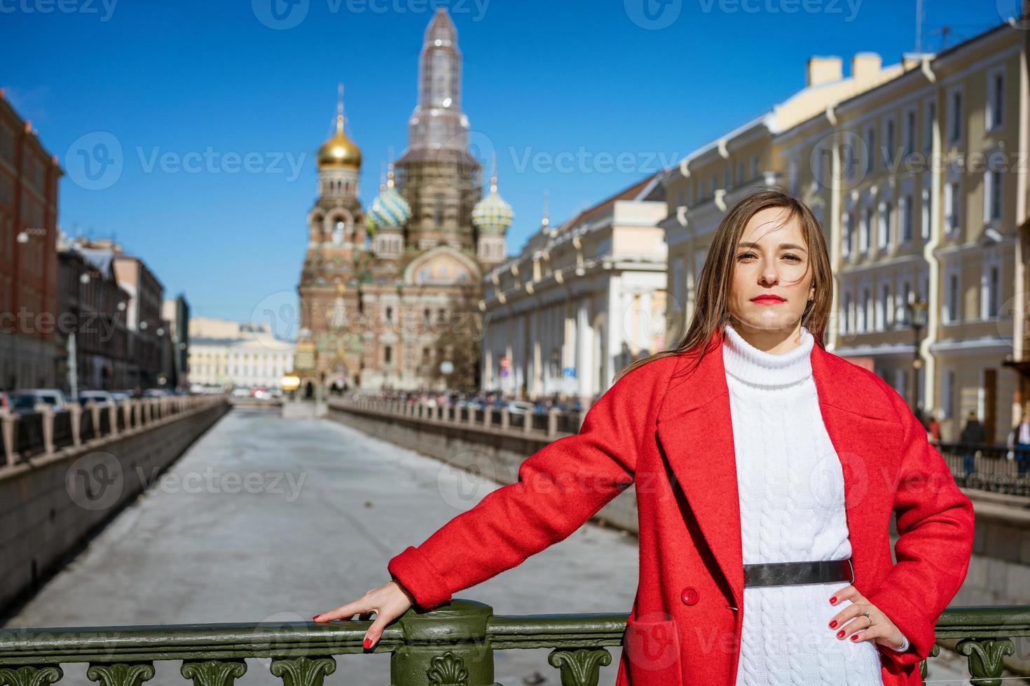 eine junge frau in einem roten mantel geht an einem sonnigen tag durch die stadt und posiert für die kamera foto