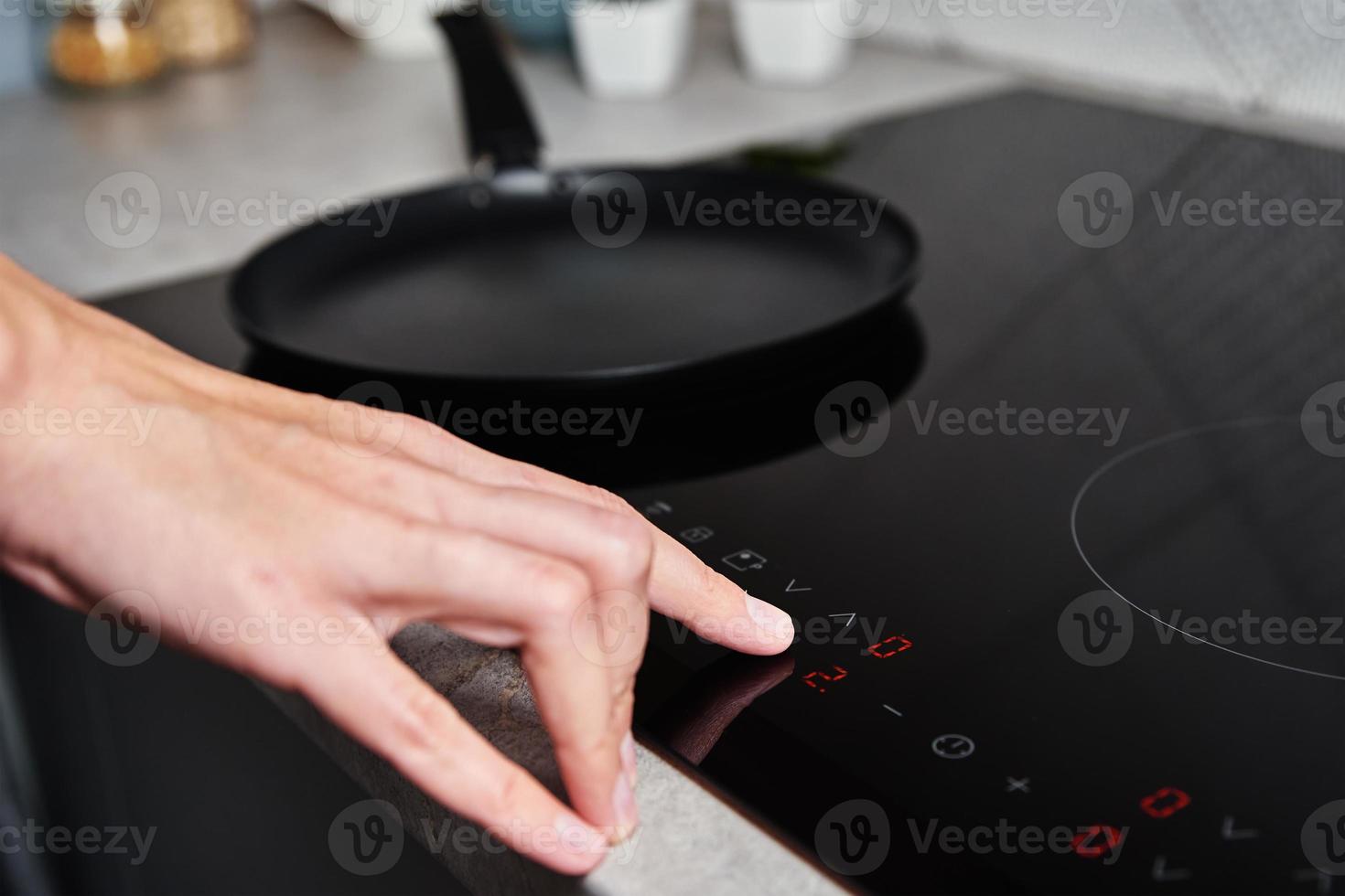 Frauenhand schaltet modernen Induktionsherd in der Küche ein foto