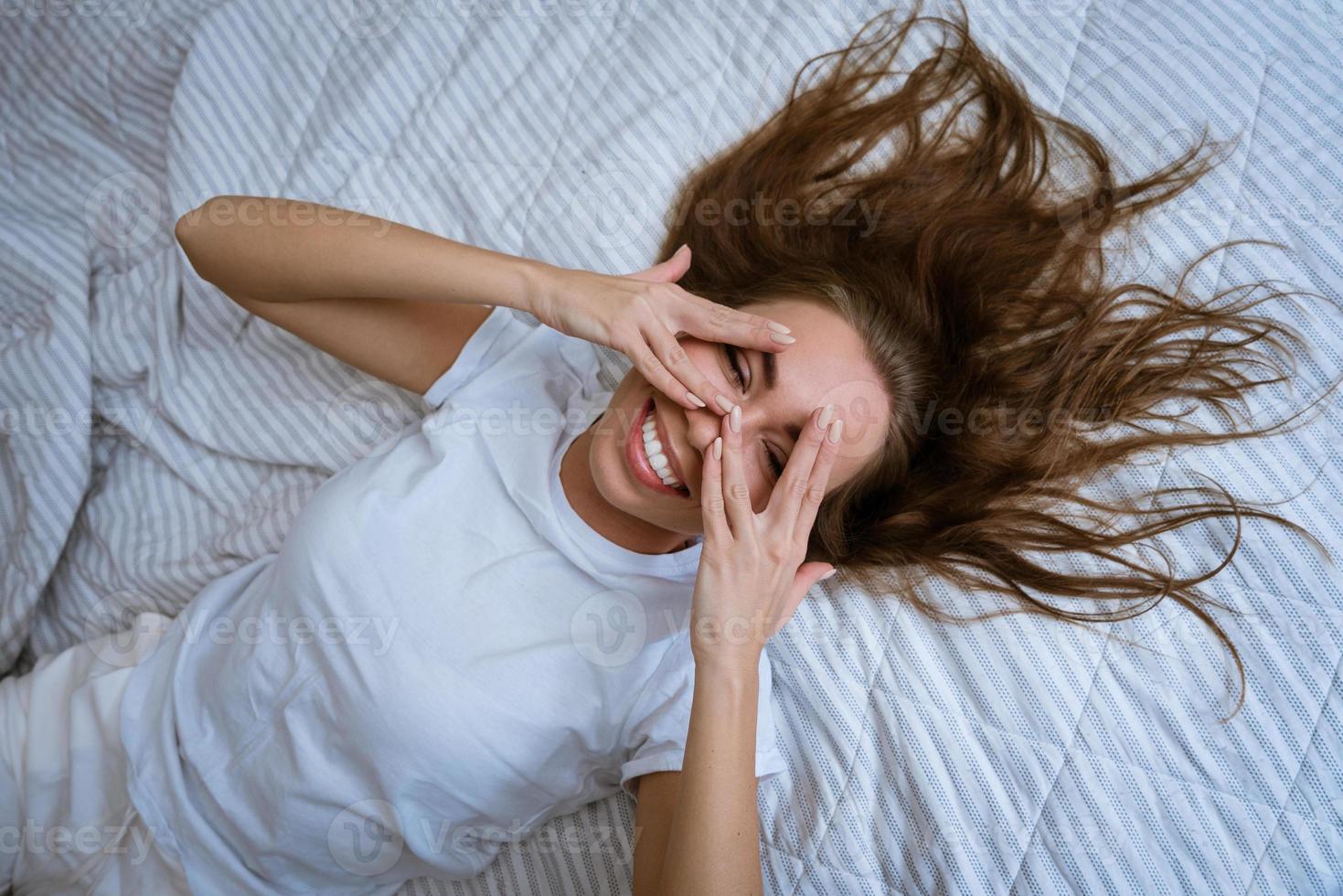 schöne junge Frau, die lächelnd im Bett liegt. foto