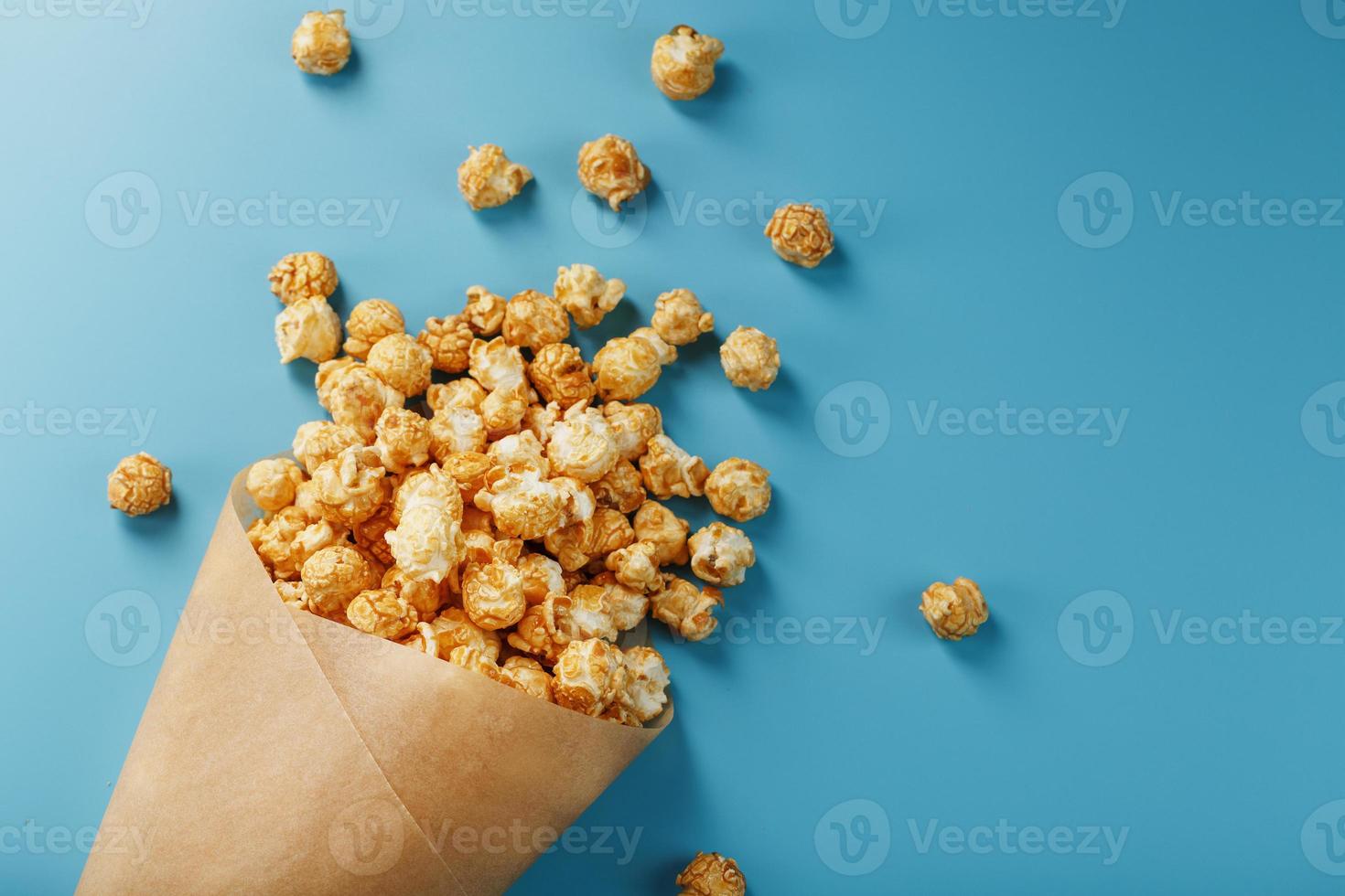 Popcorn in Karamellglasur in einem Papierumschlag auf blauem Hintergrund. foto