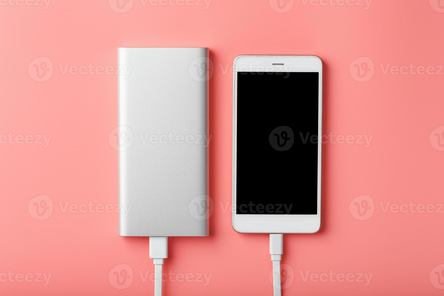 powerbank lädt ein smartphone auf einem rosa hintergrund auf. Universelle externe Batterie für Gadgets Freiraum und minimalistische Komposition. foto