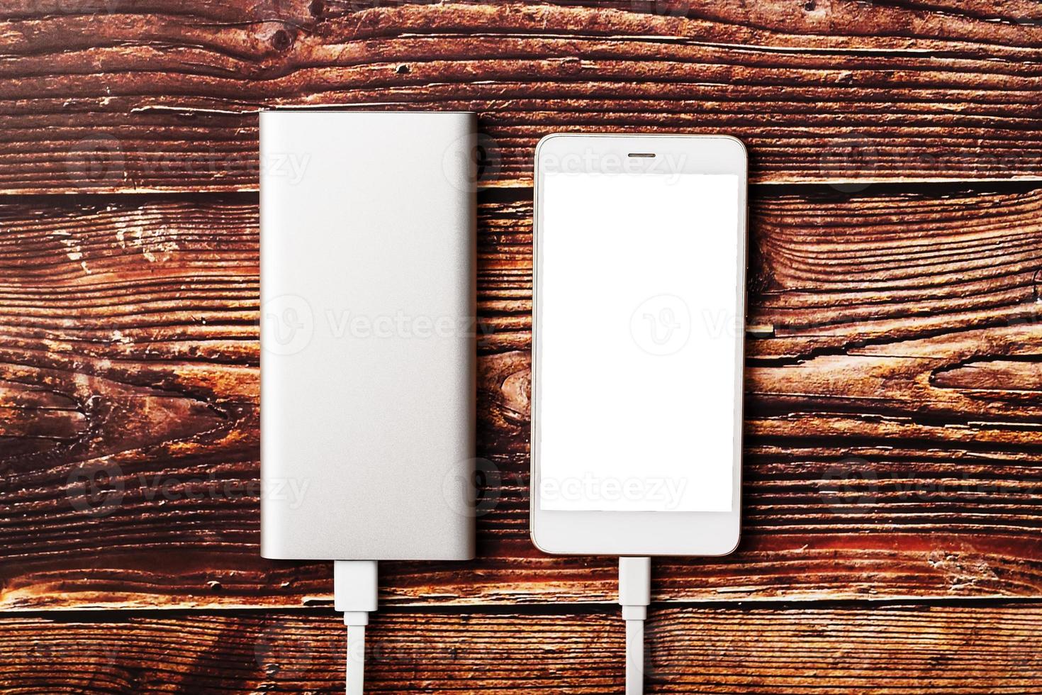 powerbank lädt ein smartphone auf einem hölzernen hintergrund auf. Universelle externe Batterie für Gadgets Freiraum und minimalistische Komposition. foto