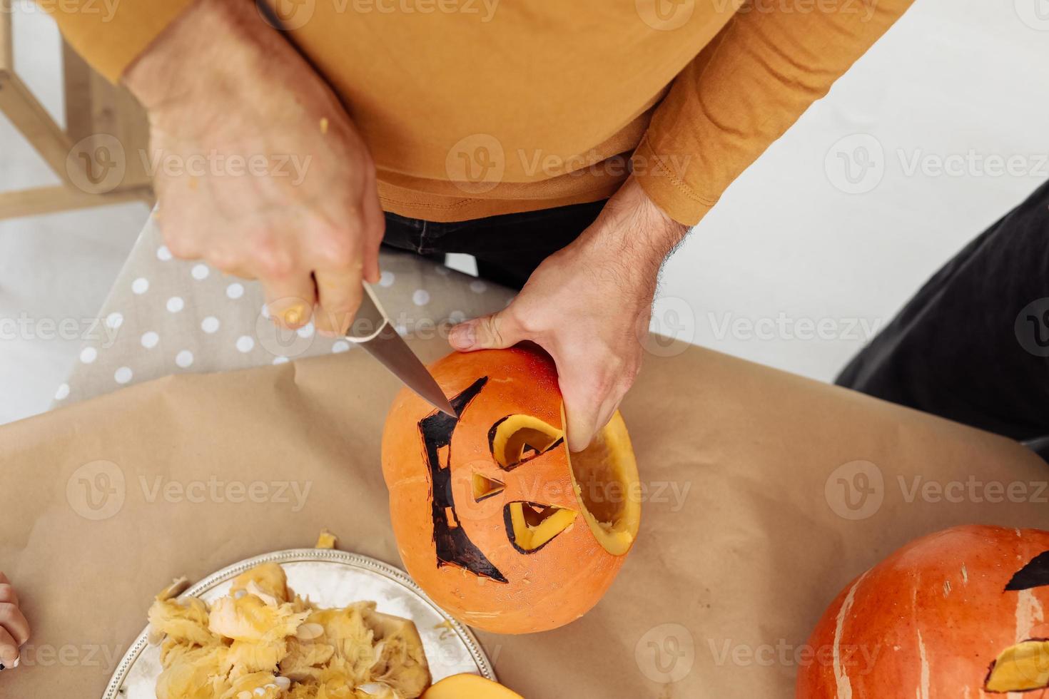 Nahaufnahme von Mannhänden, die Jack o Laternen aus reifem orangefarbenem Kürbis mit Messer auf ihrem hölzernen Küchentisch schnitzen. mann, der all hallows eve halloween partydekorationen vorbereitet. Hintergrund, Kopierbereich. foto