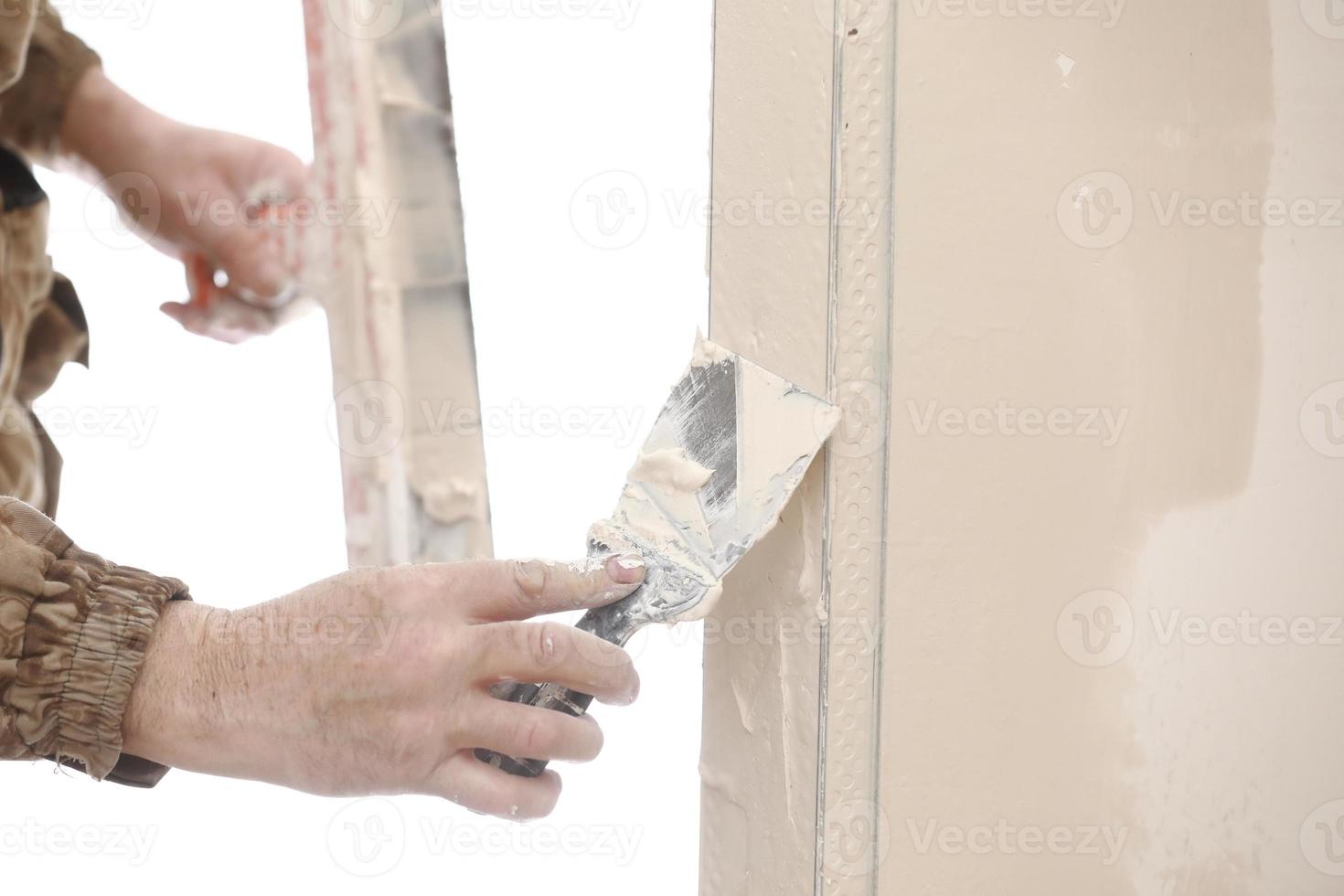 Baumeister mit einer Kelle, um Putz hinzuzufügen. Verputzwand mit Spachtel, Nahaufnahme. Befestigung der Wandoberfläche und Vorbereitung zum Streichen. Bauarbeiten während der Quarantäne foto