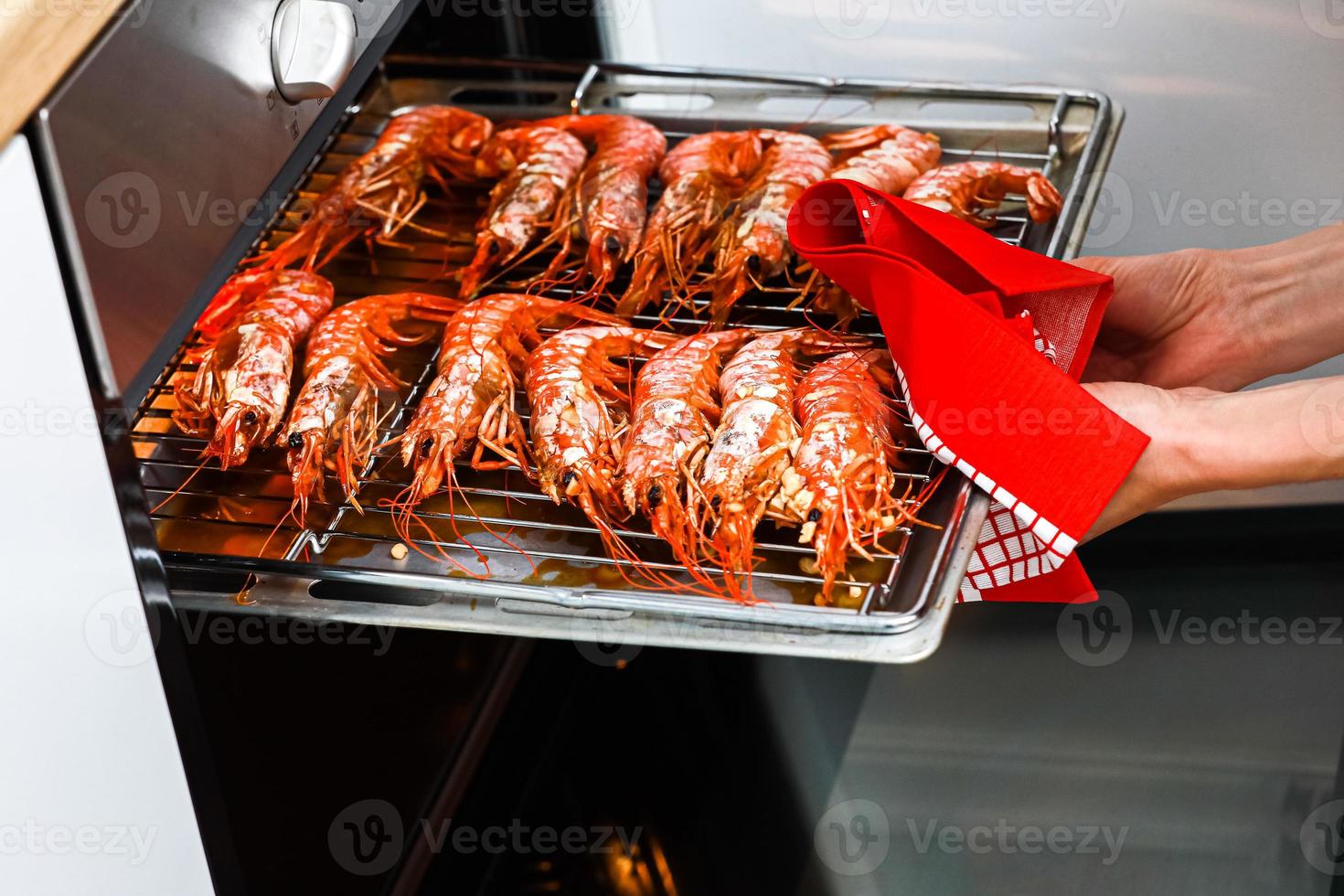 gegrillte Garnelen und gebratene Garnelen in der heimischen Küche. Frau, die einen Garnelengrill auf einem rostfreien Tablett hält und in einem Elektroofen kocht, um eine Nachtparty zu feiern. Meeresfrüchte foto