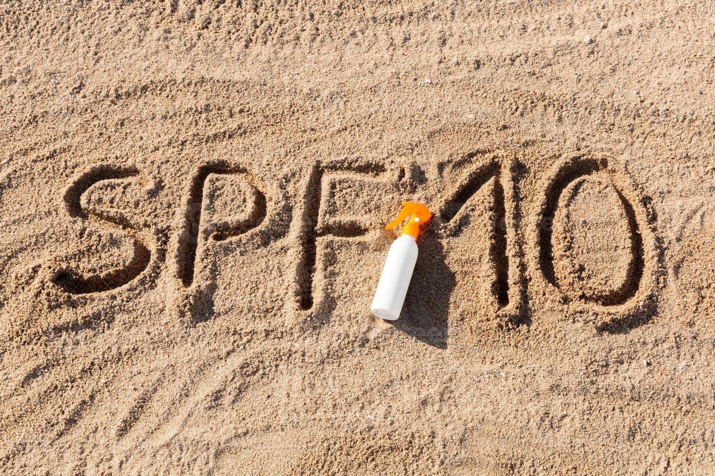 Sonnenschutzfaktor zehn. spf 10 wort geschrieben auf dem sand und der weißen flasche mit sonnencreme. hintergrund des hautpflegekonzepts foto