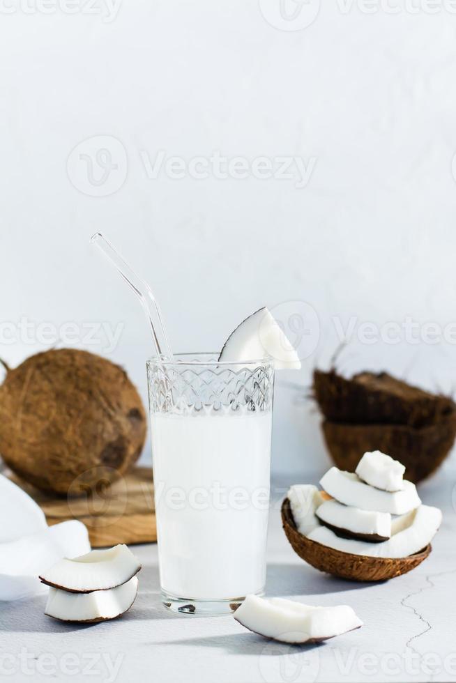 Kokosmilch in einem Glas und tropische Fruchtstücke auf dem Tisch. vertikale Ansicht foto
