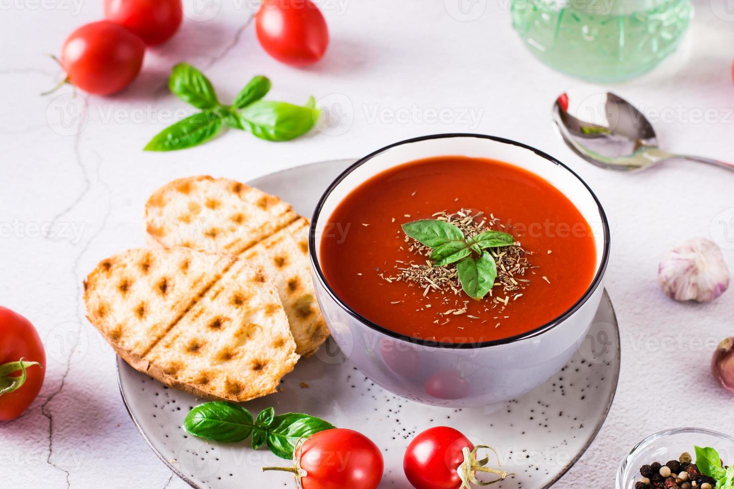 Schüssel mit hausgemachter Tomatensuppe mit Basilikum und frischem Gemüse auf dem Tisch foto