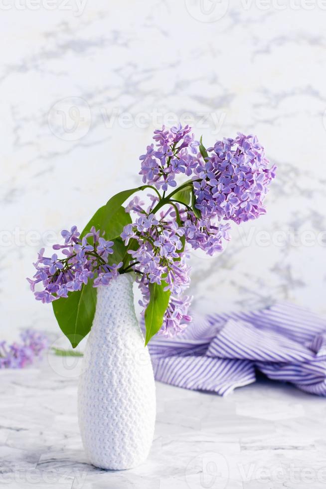 Strauß frischer Flieder in einer weißen Vase auf dem Tisch. frühlingsblühendes stillleben. vertikale Ansicht foto