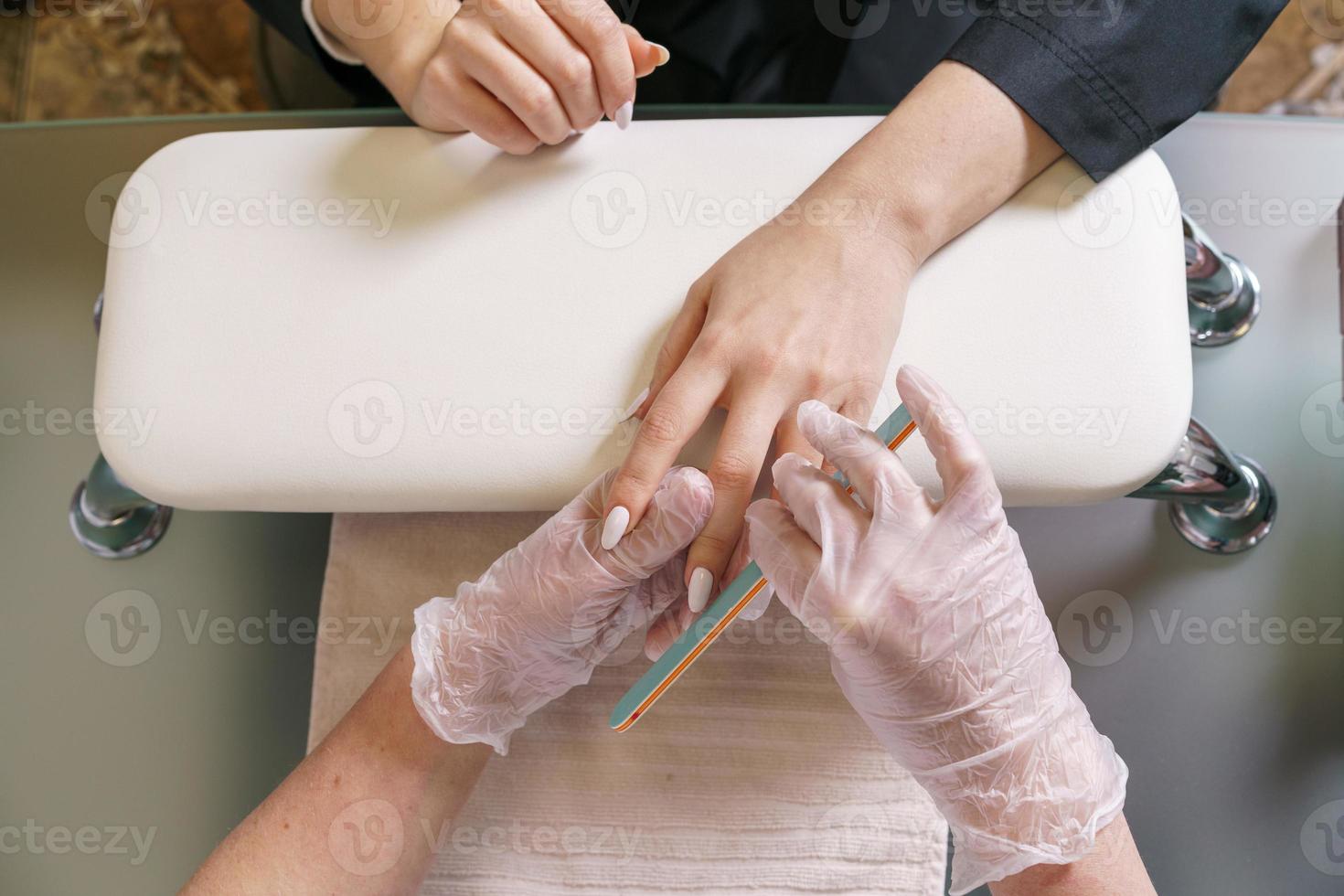 Nahaufnahme einer Frau im Nagelstudio, die Maniküre-Kosmetikerin mit Nagelfeile macht foto