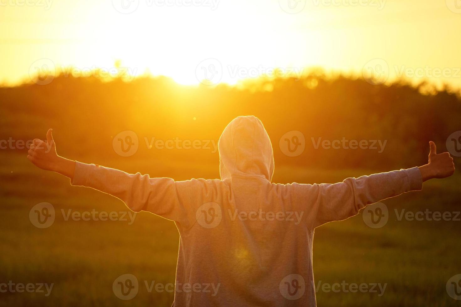 Ein Mann im Licht des Sonnenuntergangs mit erhobenen Händen, das Konzept von Erfolg, Freiheit und Freude foto