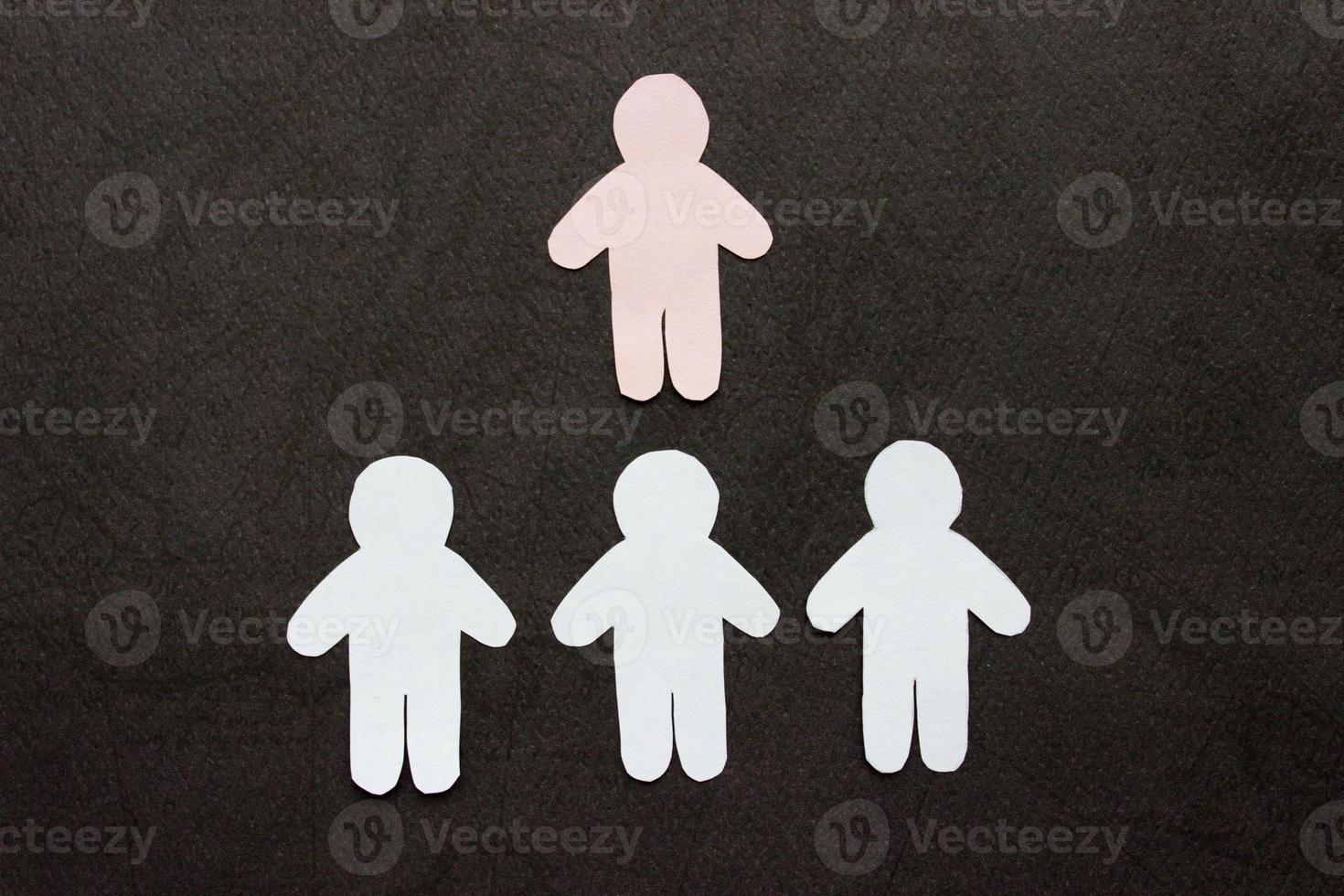 Silhouetten von drei Männern, in einer Reihe angeordnet, aus Papier geschnitten. über ihnen ist ein rosa Mann. auf schwarzem Hintergrund. Konzept Führung, Kommunikation, Macht, Einzigartigkeit, Business foto