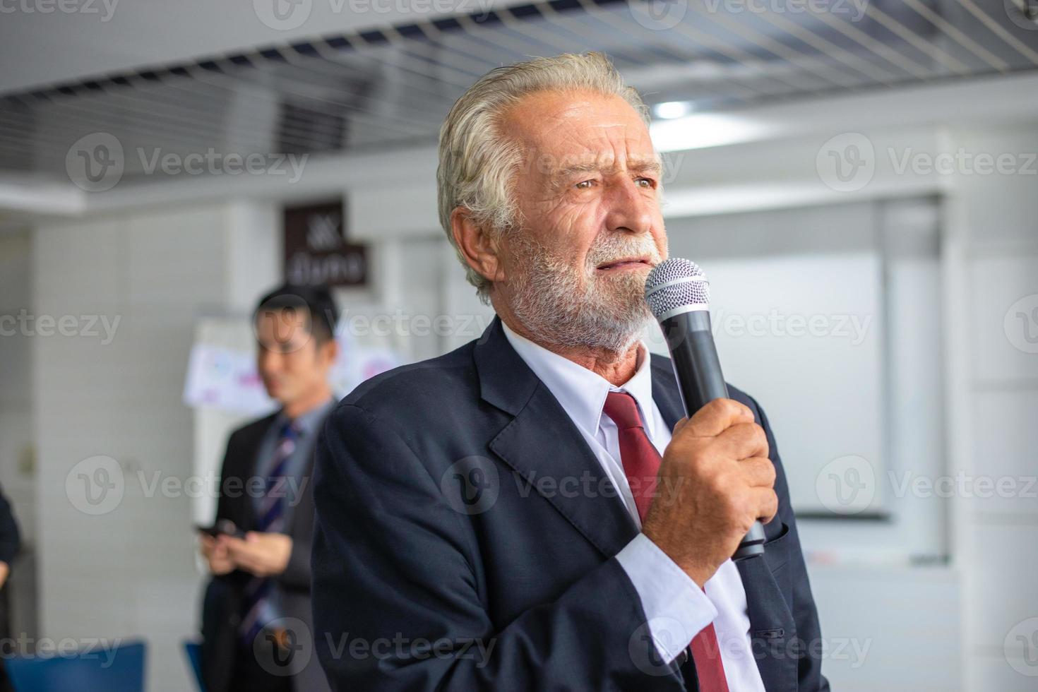 älterer geschäftsmann, der ein mikrofon hält, das bei einem treffen spricht foto