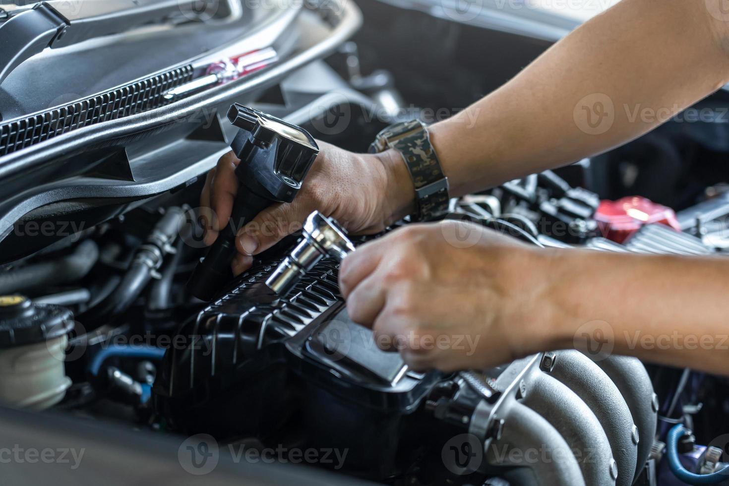 Schließen Sie die Zündkerzenspule an der Motorabdeckung und ein Mann verwendet einen Blockschlüssel, um eine Schraube für den Motorservice der Startspule in der Garage und im Hintergrund des Maschinenraums zu entfernen foto