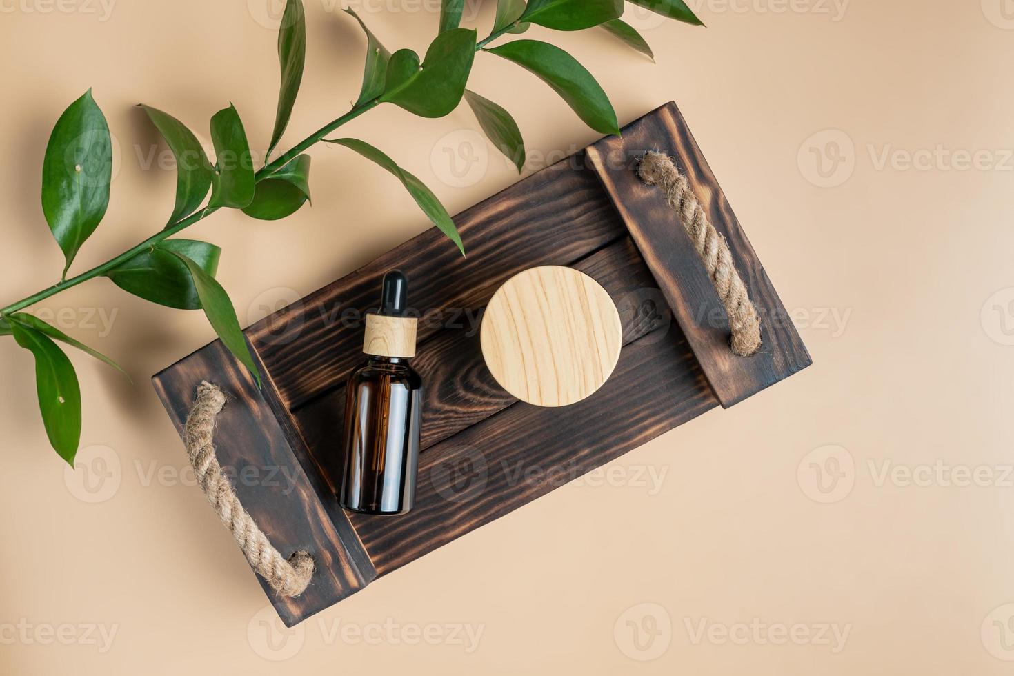 Ätherisches Gesichtsöl oder Serum- und Cremeglas mit Bambusdeckelverpackung auf Holztablett auf beigem Hintergrund. Beauty-Kosmetikprodukt für Hautpflegekonzept. foto