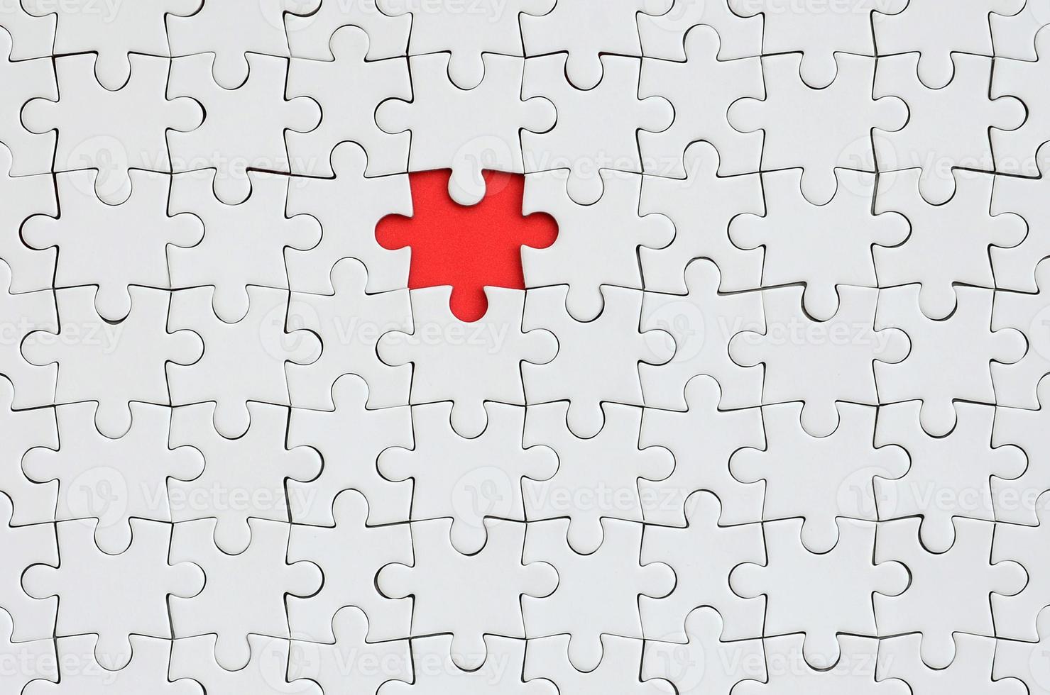 die Textur eines weißen Puzzles im zusammengebauten Zustand mit einem fehlenden Element, das einen roten Raum bildet foto