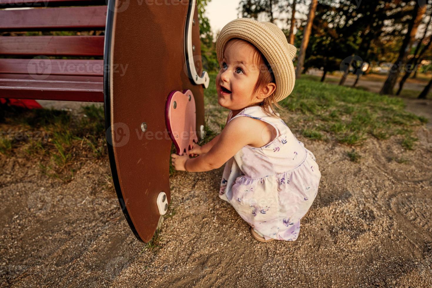 Babymädchen mit Panamahut setzte sich an die Bank auf dem Spielplatz im Freien. foto