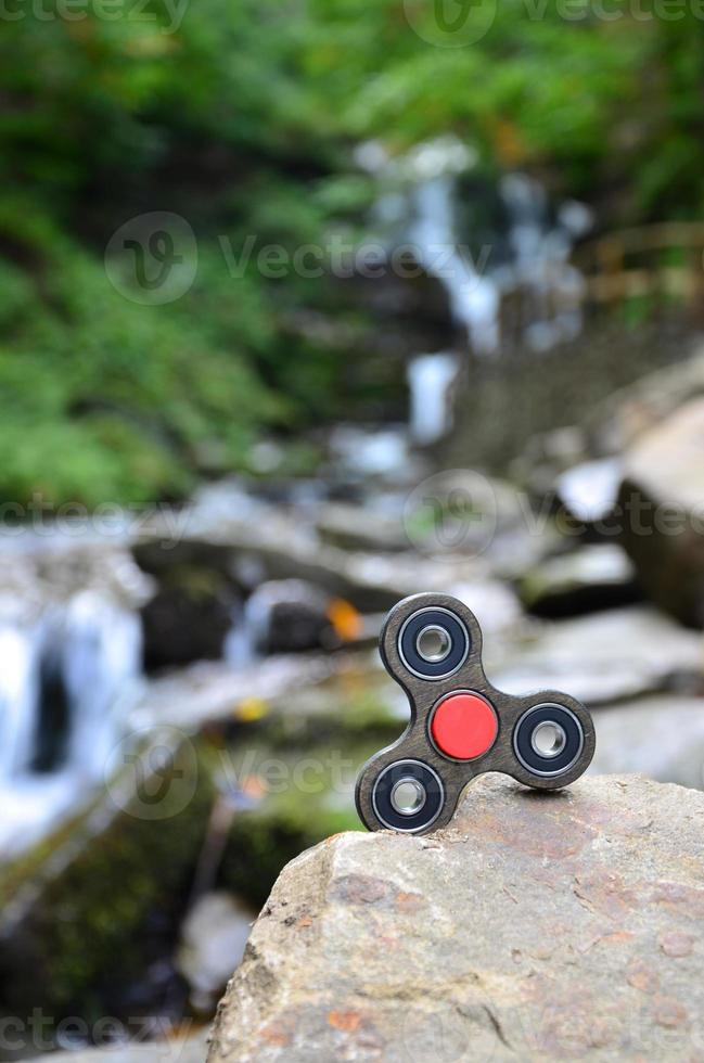 Der hölzerne Spinner liegt auf den Felsen vor dem Hintergrund eines kleinen Wasserfalls und eines Flusses foto