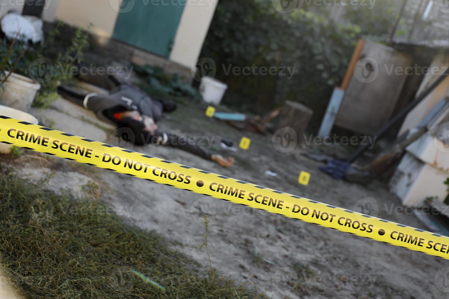 Opfer eines Gewaltverbrechens in einem Hinterhof eines Wohnhauses am Abend. Leiche eines toten Mannes unter dem gelben Polizeiband und Beweismarkierungen am Tatort foto