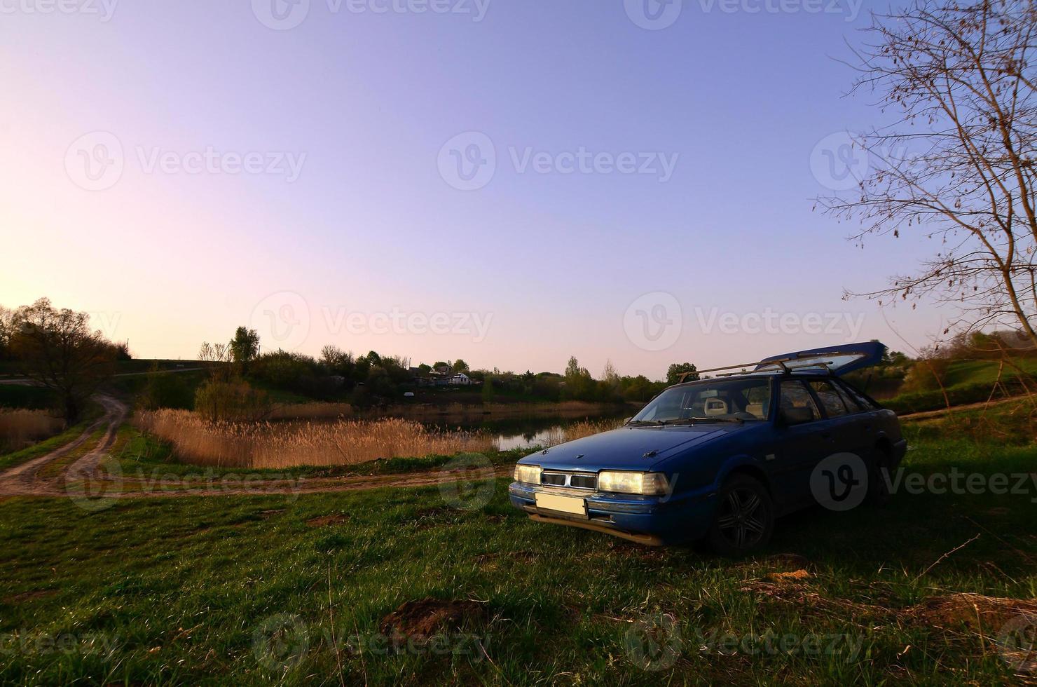 Ein blaues Auto vor dem Hintergrund einer rustikalen Landschaft mit einem wilden Zuckerrohrfeld und einem kleinen See. Die Familie kam in der Natur in der Nähe des Sees zur Ruhe foto