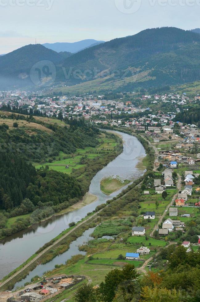 eine schöne aussicht auf das dorf mezhgorye, karpatengebiet. Viele Wohngebäude, umgeben von hohen Waldbergen und einem langen Fluss foto