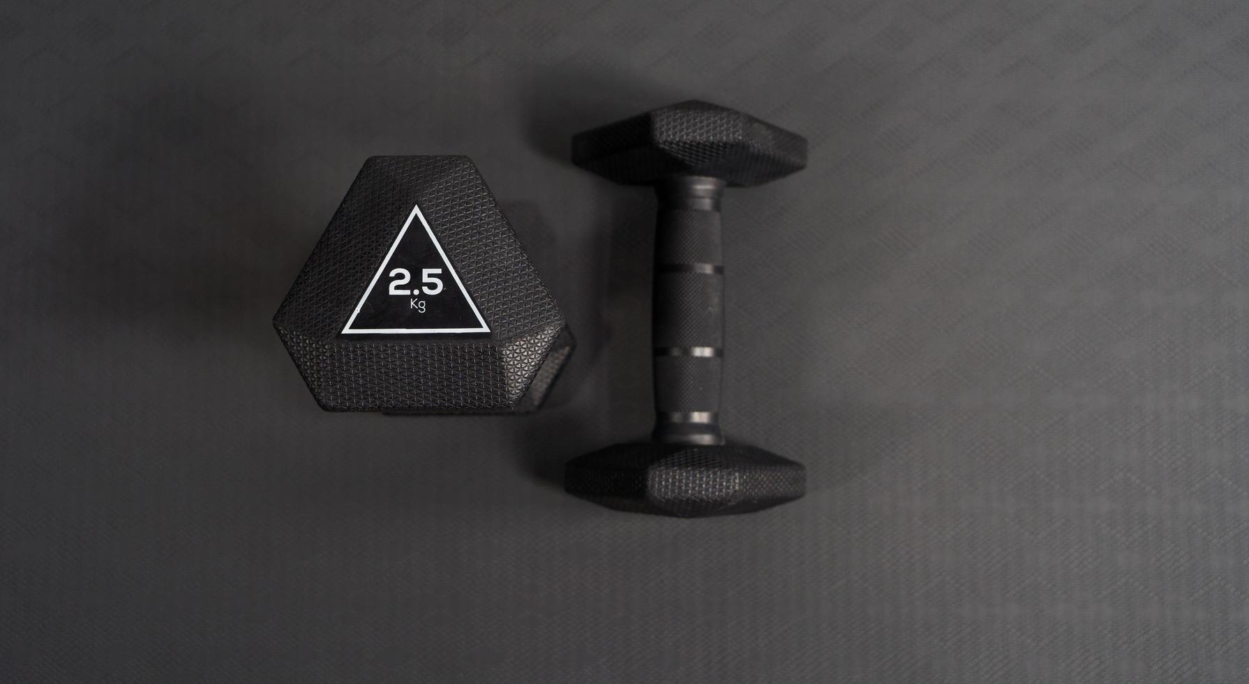 Foto von 2,5 kg schwarzer Hantel, Draufsicht auf schwarzem Gummihintergrund. Hintergrundkonzept für Fitnessgeräte
