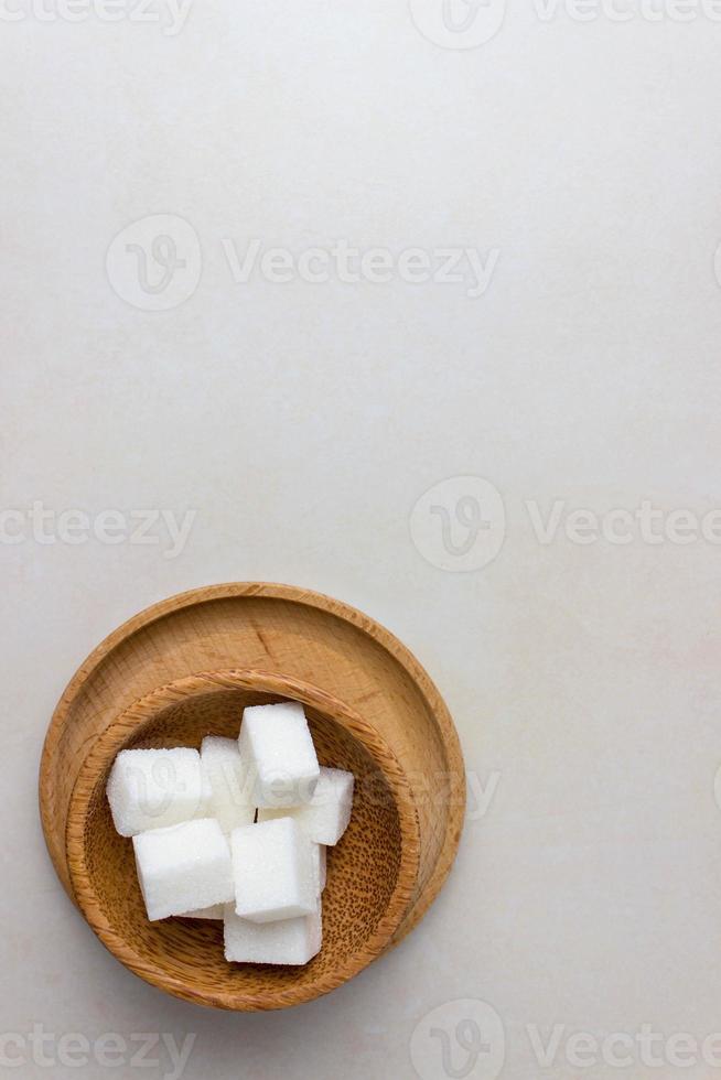 Zuckerwürfel in einem Holzteller auf dem Küchentisch. Draufsicht, vertikales Foto. mit Kopierbereich foto