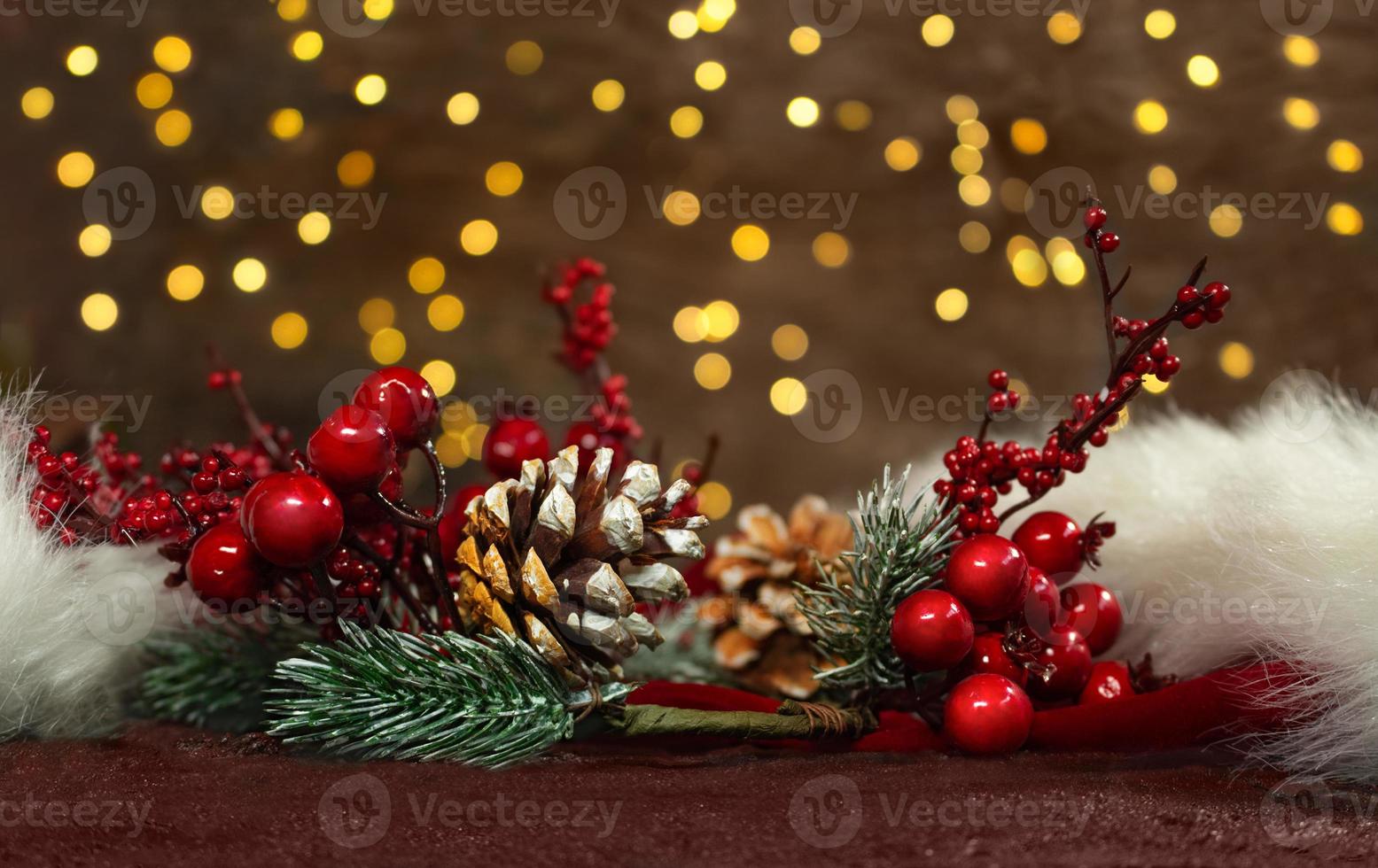 Fichtenzweige mit roten Beeren und Tannenzapfen auf einem roten Weihnachtsmann-Hut mit Neujahrslichtern im Rücken. unscharfer Hintergrund. Weihnachtskarte foto