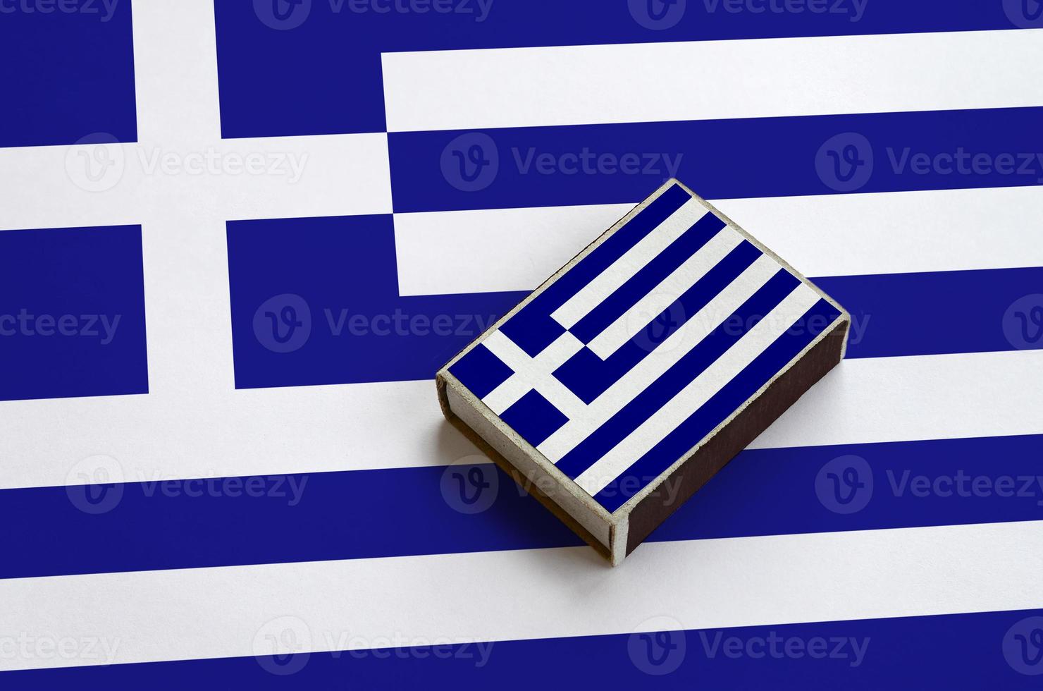 Die griechische Flagge ist auf einer Streichholzschachtel abgebildet, die auf einer großen Flagge liegt foto