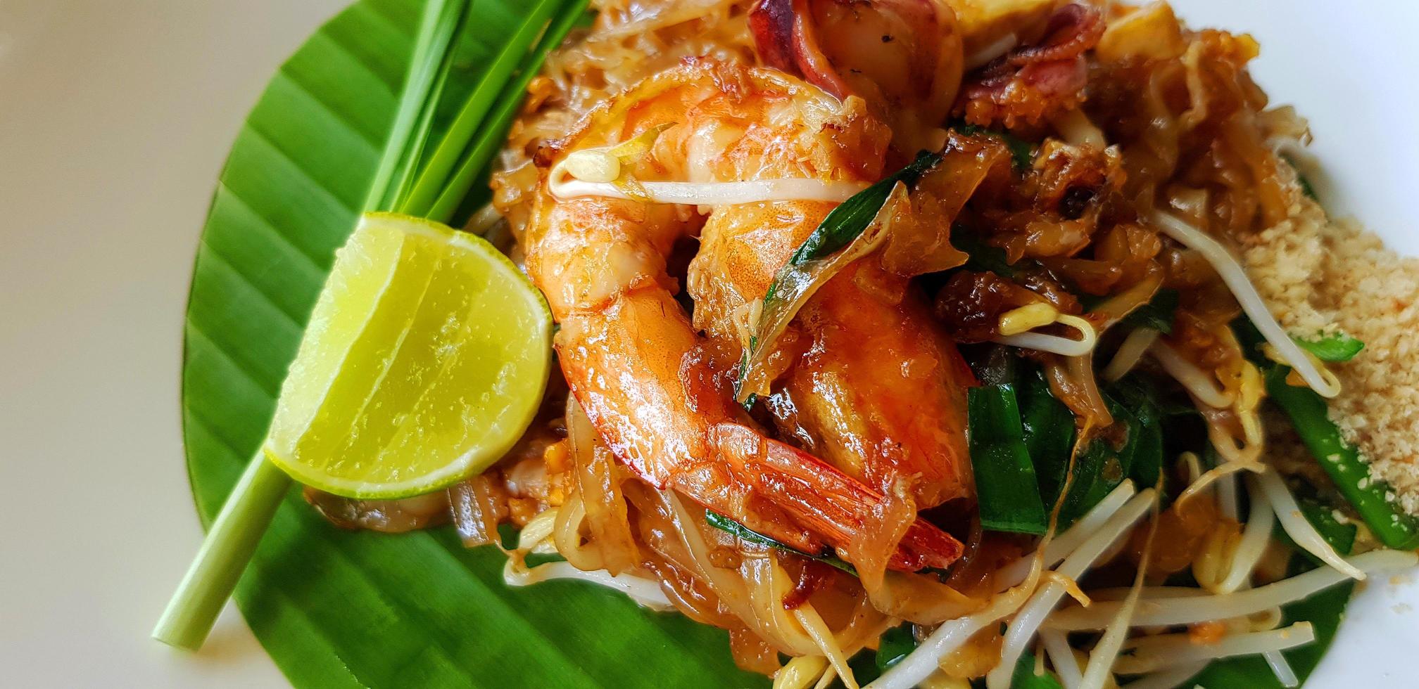 Nahaufnahme gebraten mit Reisnudeln, Flussgarnelen oder Garnelen, Sojasprossen, geschnittenem Schnittlauch und Limette auf Bananenblatt mit Kopierraum. berühmtes essen in thailand call pad thai. Technik des selektiven Fokus. foto