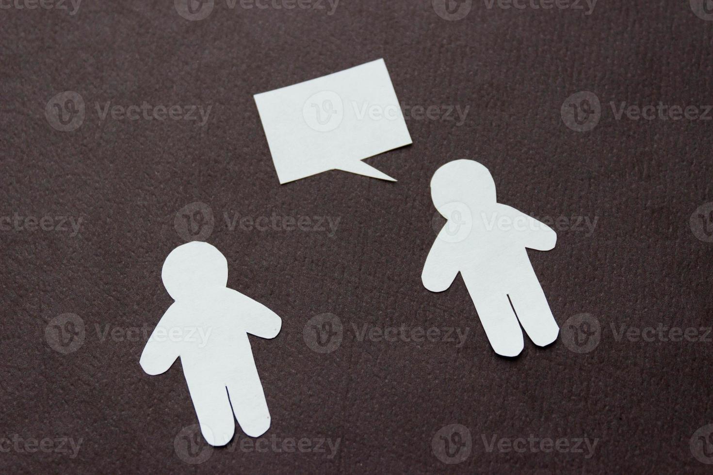 Silhouetten von zwei Personen aus weißem Papier auf schwarzem Hintergrund. Menschen stehen sich gegenüber, einer spricht Sprechblase . Kommunikation, Führung, Partnerschaft, Teamarbeit etc. foto