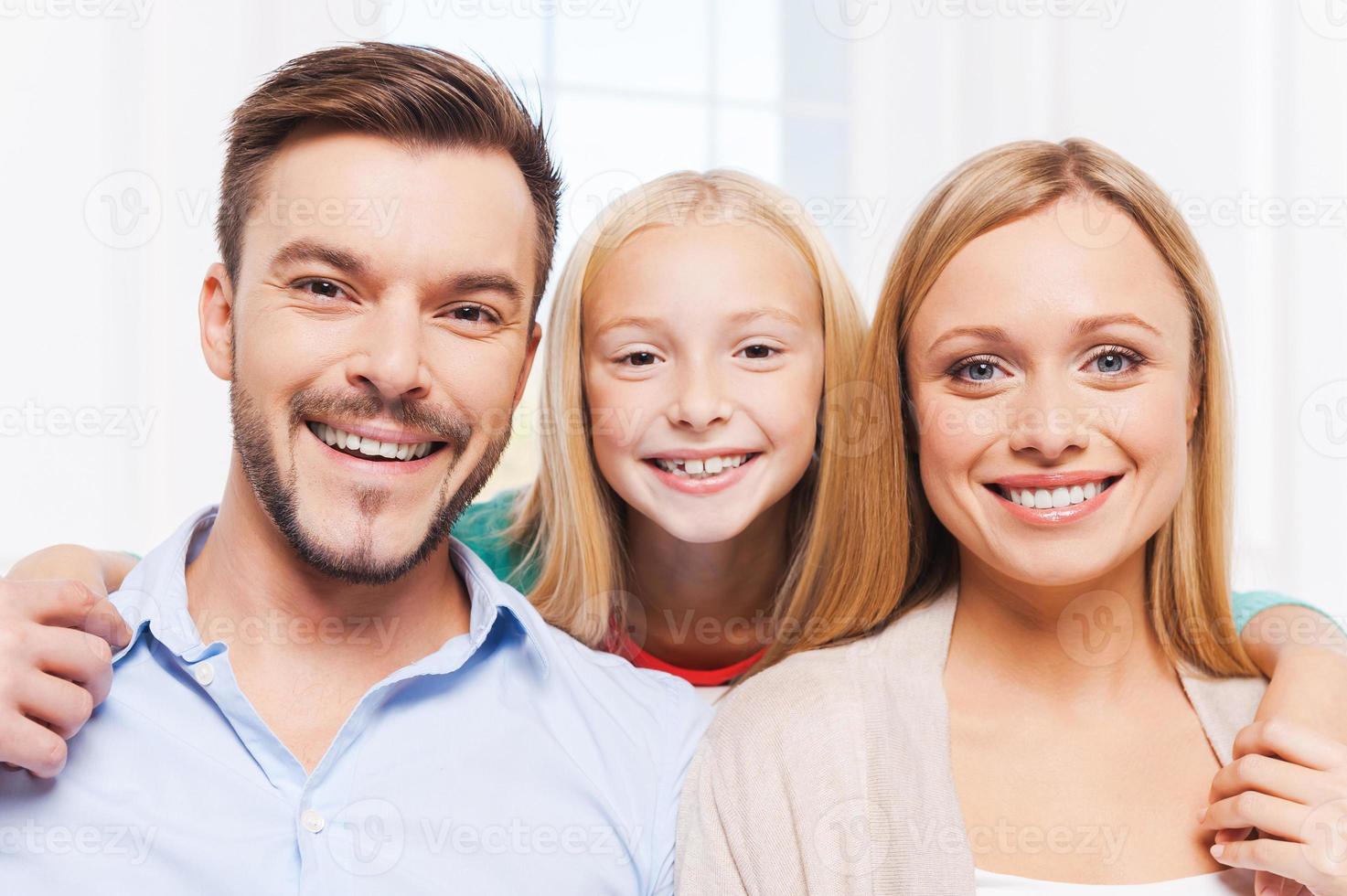 glückliche Familie. glückliche dreiköpfige Familie, die sich aneinander bindet und lächelt, während sie drinnen sitzt foto