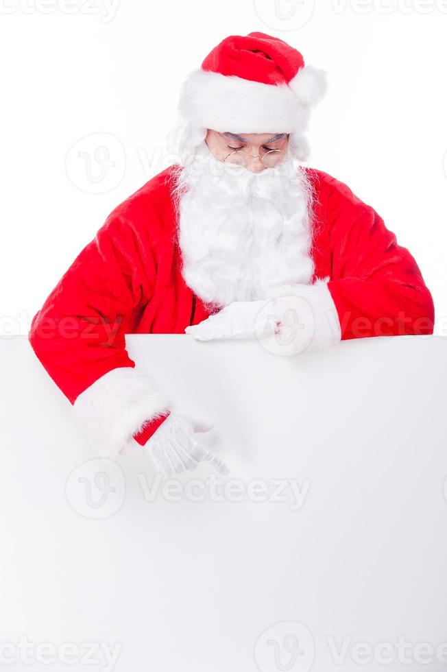 neugieriger Weihnachtsmann. traditioneller weihnachtsmann, der kopienraum zeigt, während er vor weißem hintergrund steht foto