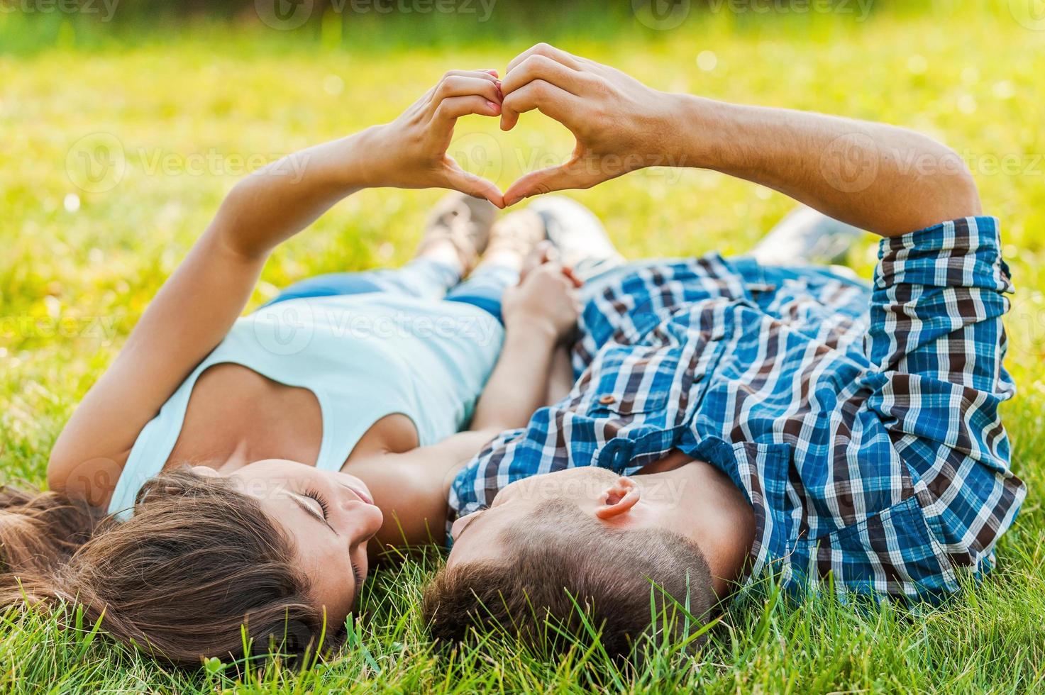 Symbol der Liebe. Paare, die Herzform mit den Händen machen und auf dem Gras liegen foto