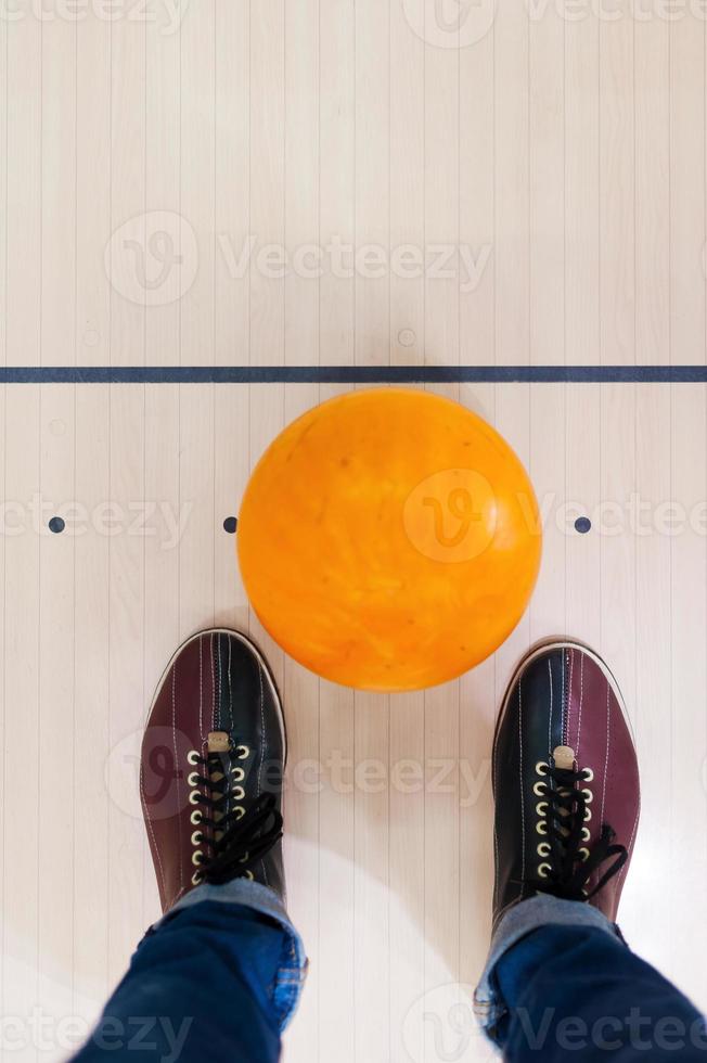 bereit für ein Spiel. Nahaufnahme einer Bowlingkugel, die in der Nähe menschlicher Beine liegt foto