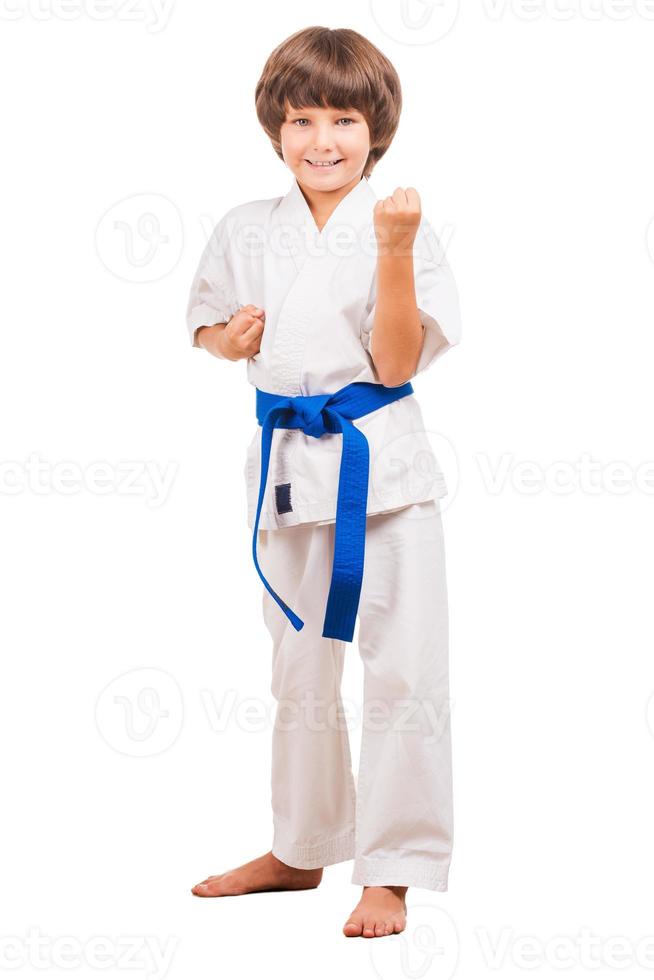 Ich kann mich verteidigen. voller Länge des kleinen Jungen in Karate-Uniform, der in Karate-Position steht, während er isoliert auf Weiß steht foto