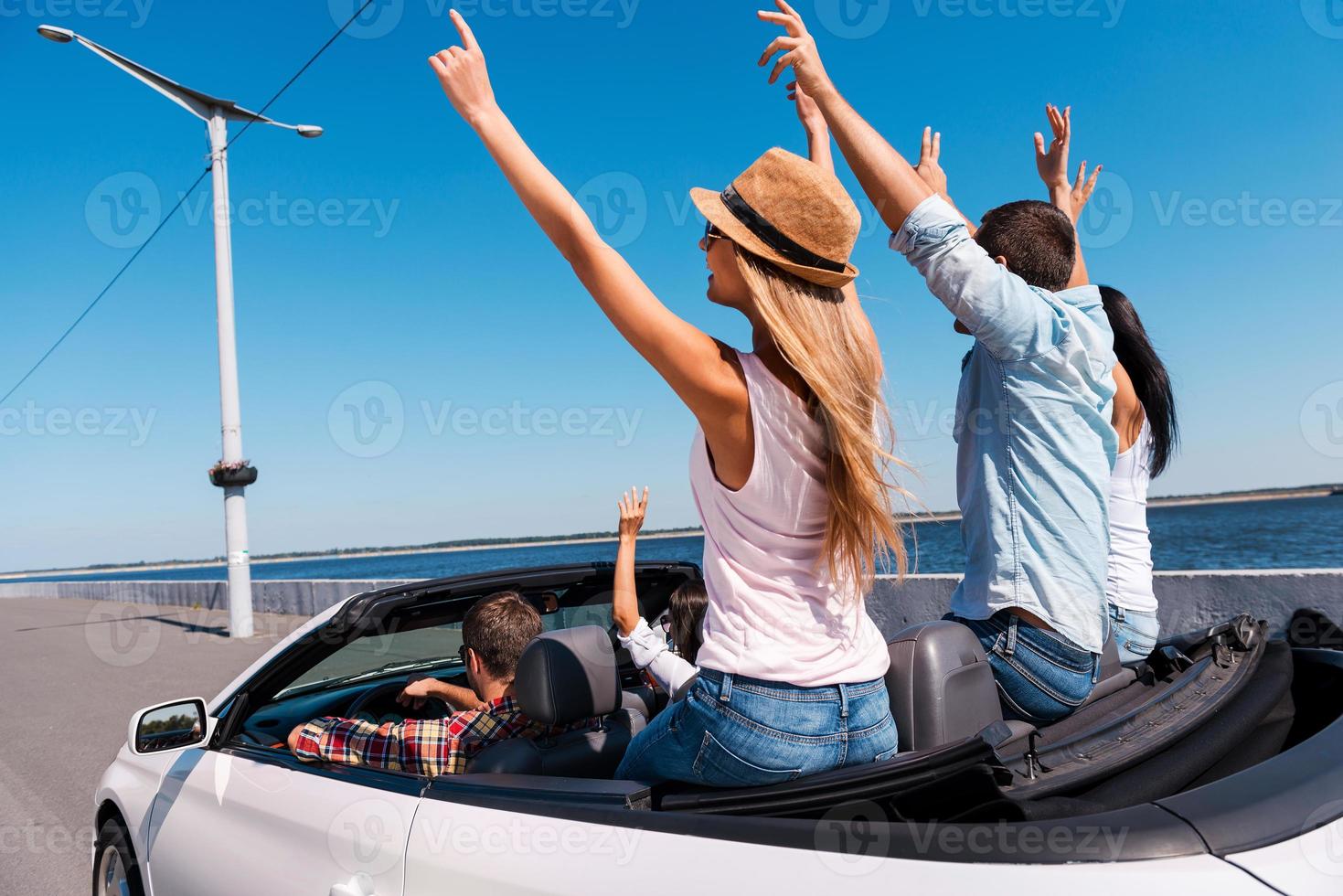 zusammen reisen macht großen spaß. Rückansicht junger glücklicher Menschen, die in ihrem Cabrio unterwegs sind und die Arme hochheben foto