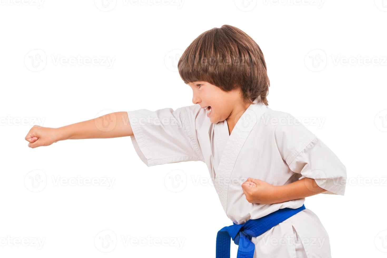 Karate Kid. Seitenansicht des kleinen Jungen, der Kampfkunstbewegungen macht, während er isoliert auf weißem Hintergrund ist foto