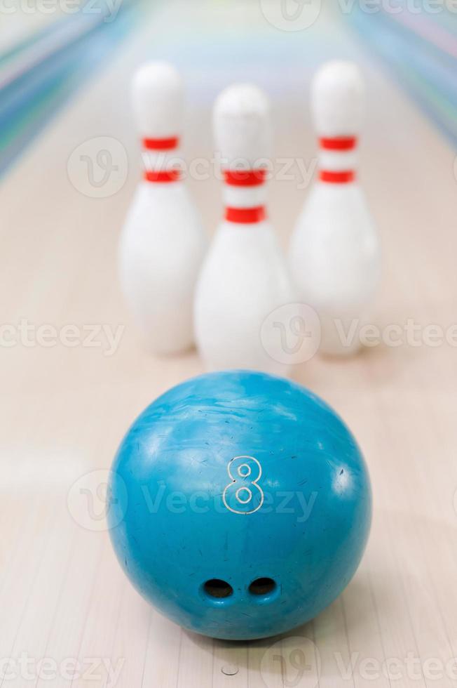 Pins und Ball sind ein tolles Team. Nahaufnahme der blauen Bowlingkugel, die gegen Stifte liegt, die auf der Bowlingbahn bleiben foto