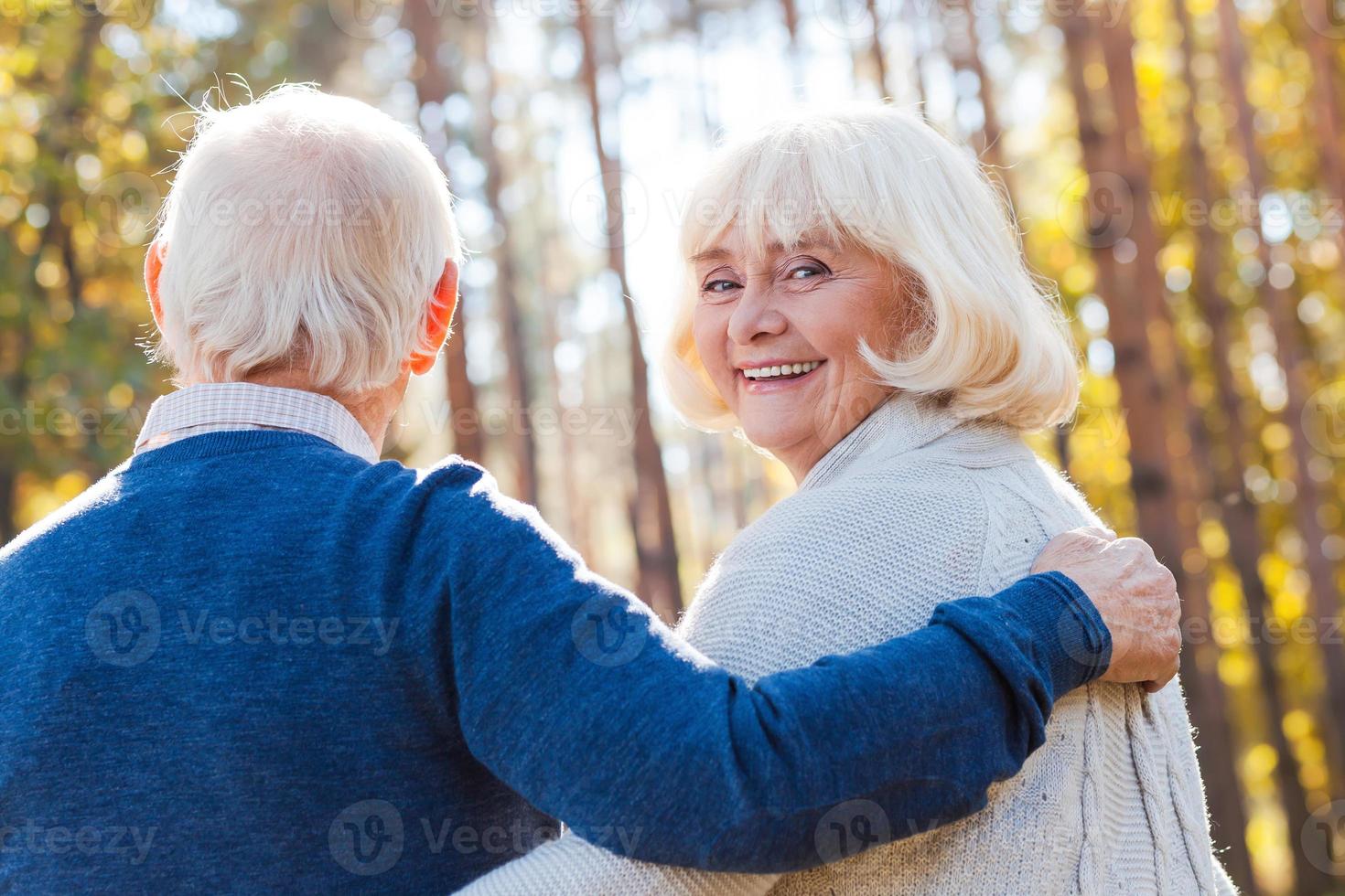 Zeit mit Ehemann verbringen. Rückansicht einer glücklichen Seniorin, die über die Schulter schaut und lächelt, während sie mit ihrem Mann durch den Park geht foto