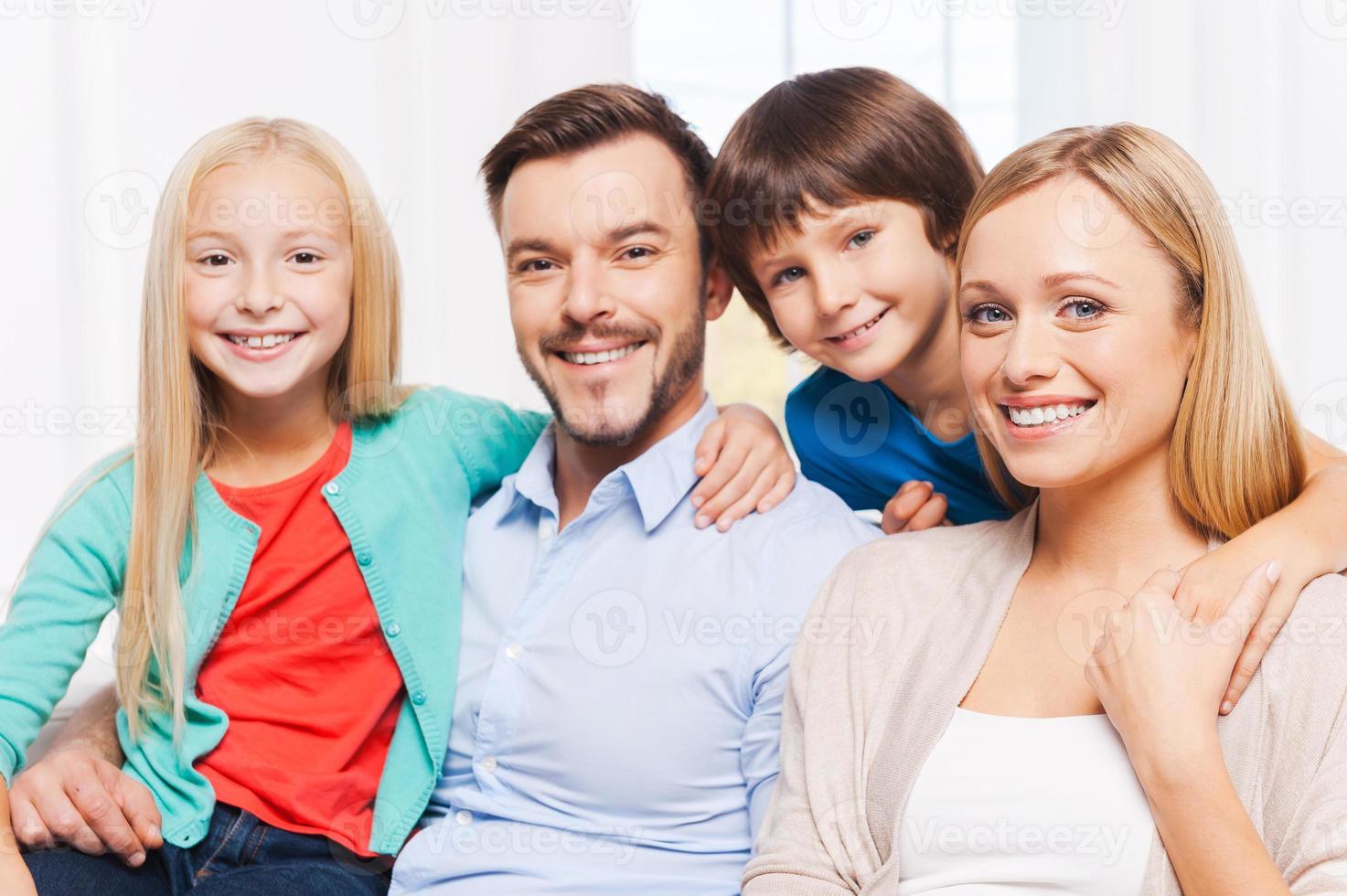 glücklich, eine Familie zu sein. glückliche vierköpfige Familie, die sich aneinander bindet und lächelt, während sie drinnen sitzt foto